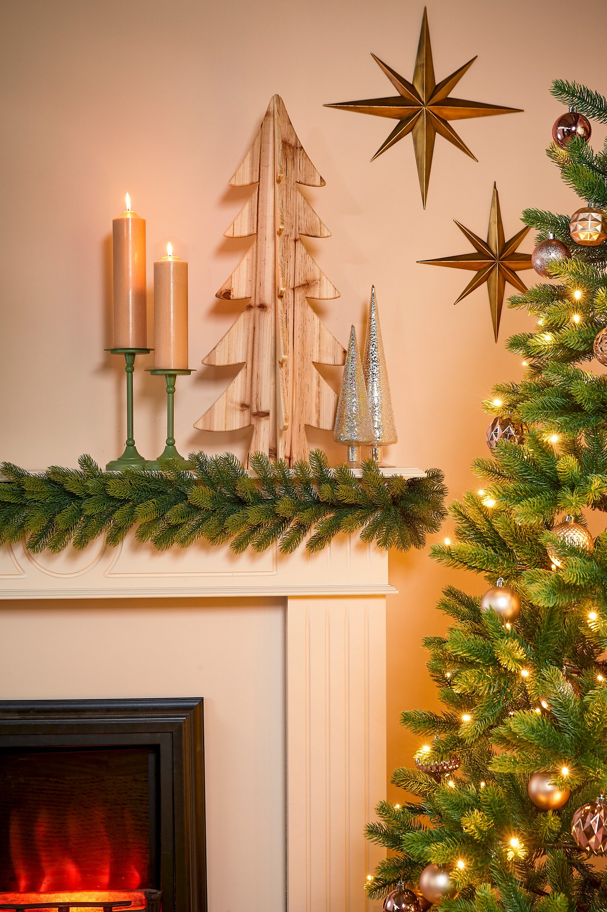 Une scène de Noël décorée avec un arbre, des bougies et des étoiles sur le mur. Une cheminée est au premier plan.