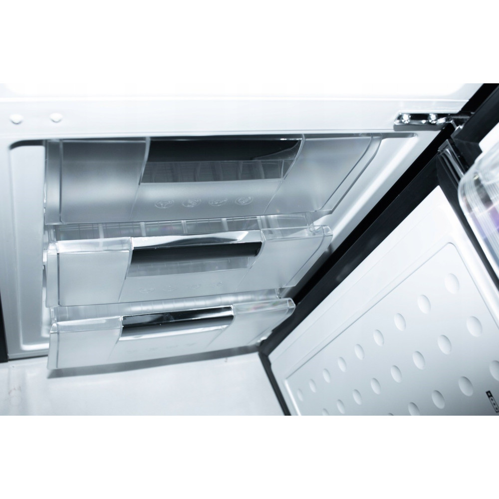 Wewnątrz lodówki wysunięte są dwie przezroczyste szuflady. Drzwi są otwarte. Białe wnętrze z czarnym obramowaniem.