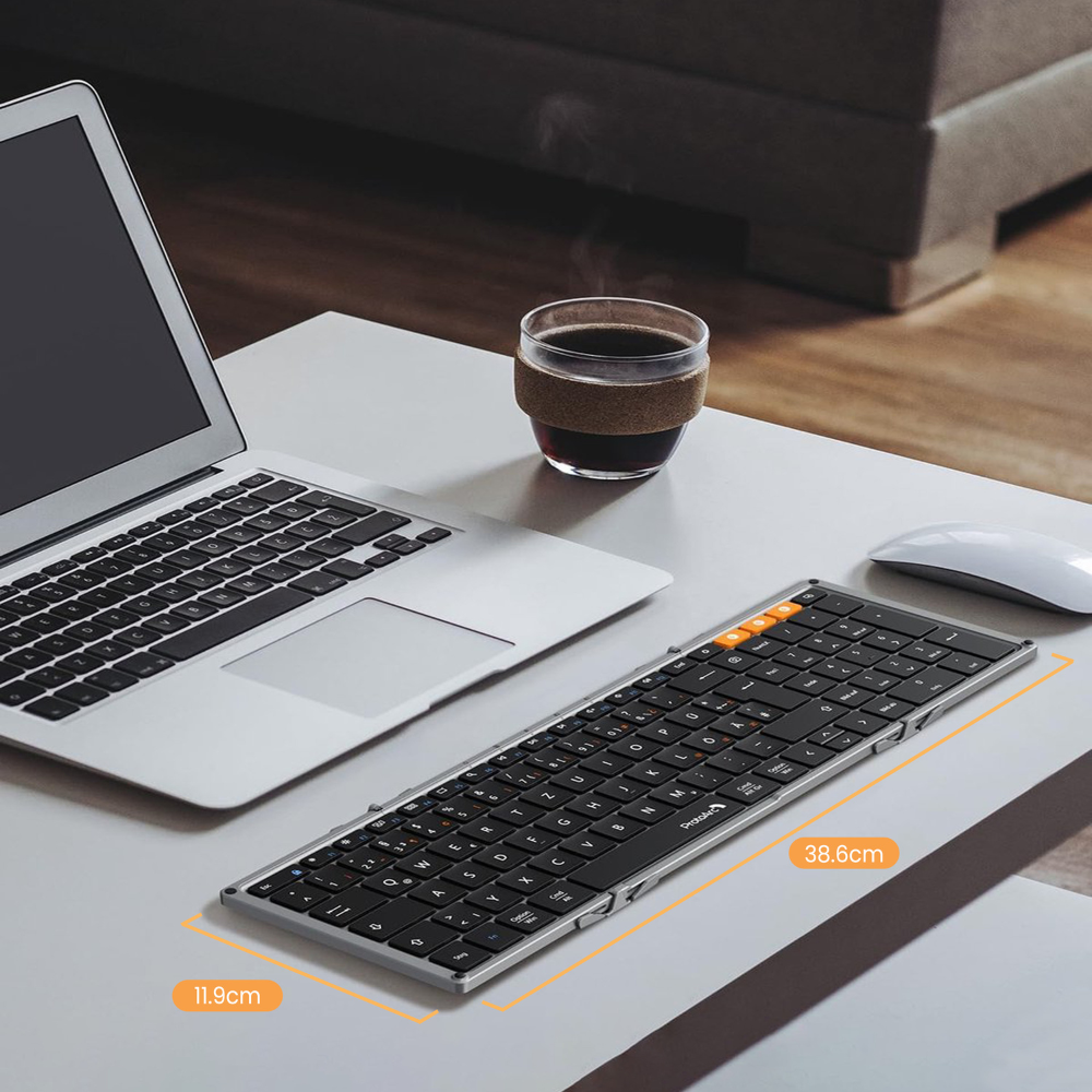 Ein Laptop, eine schwarze Tastatur, eine Tasse Kaffee und eine Maus liegen auf einem Schreibtisch. Abmessungen der Tastatur sind 38,6 cm x 11,9 cm.