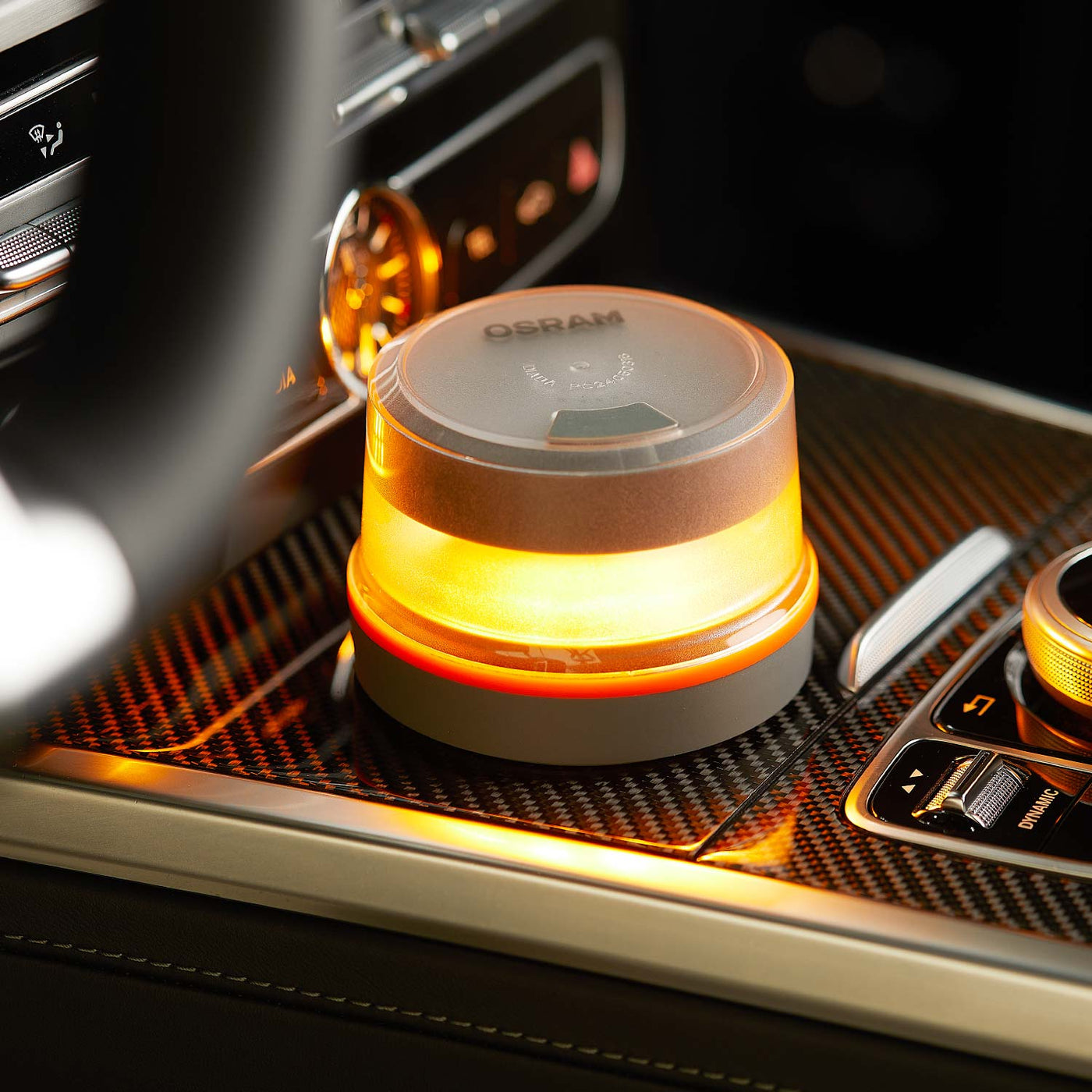 Una luz de advertencia Osram iluminada se encuentra en la consola de un automóvil. La luz es naranja, con base gris y cubierta transparente.