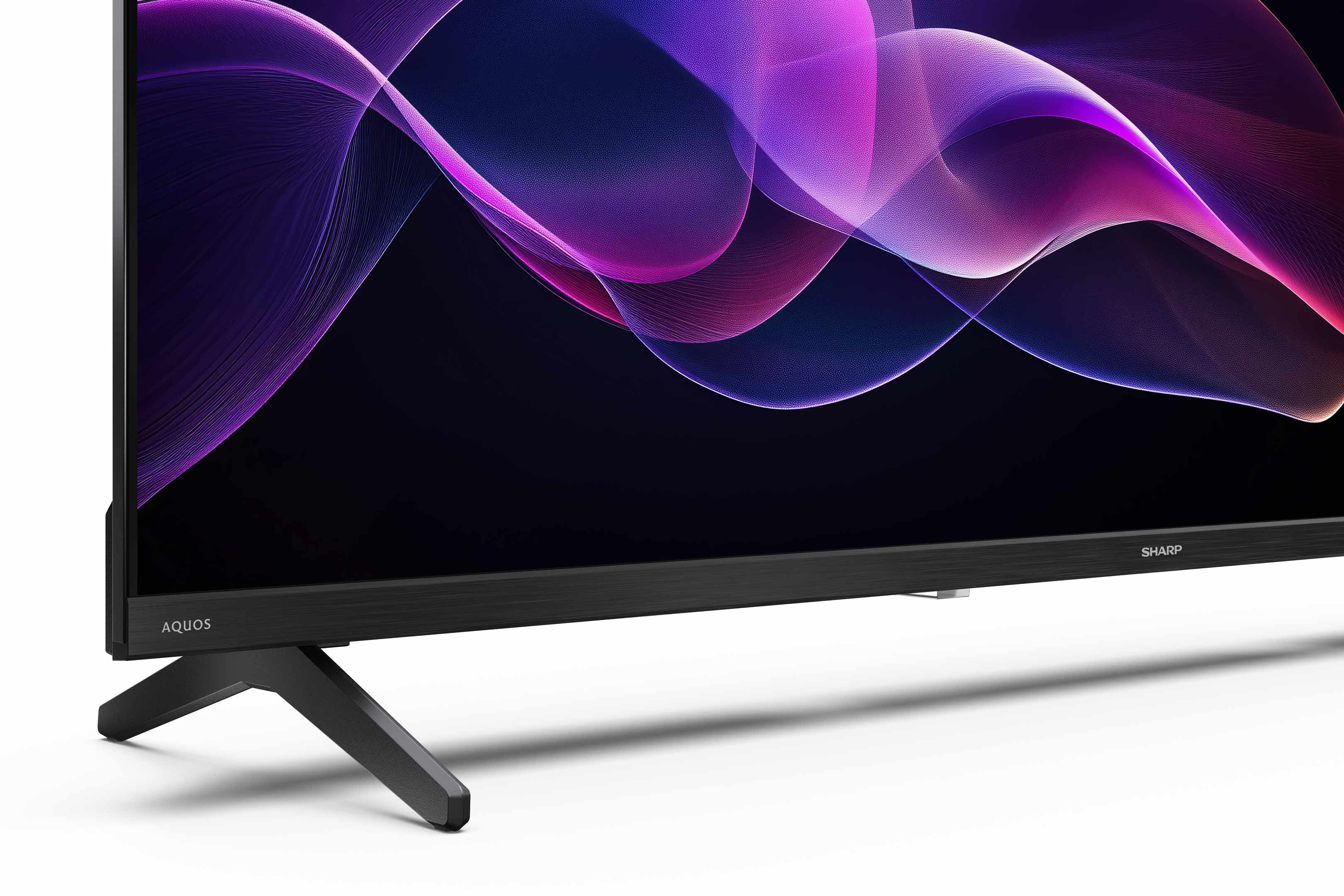 Ein Sharp Aquos Fernseher. Der Bildschirm zeigt abstrakte lila und rosa Formen. Der Fernseher hat einen schwarzen Ständer.
