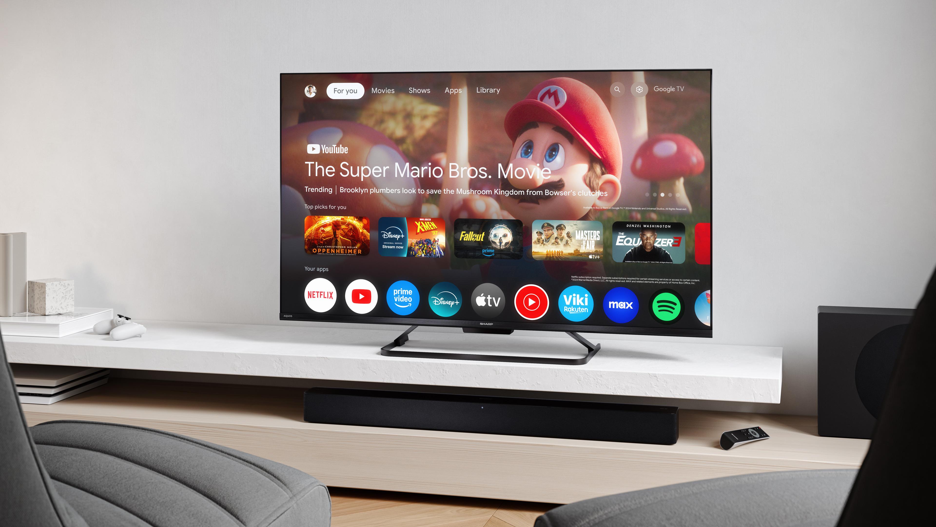 Telewizor wyświetla 'The Super Mario Bros. Movie'. Widoczne są aplikacje, jak Netflix i YouTube. Soundbar i pilot.