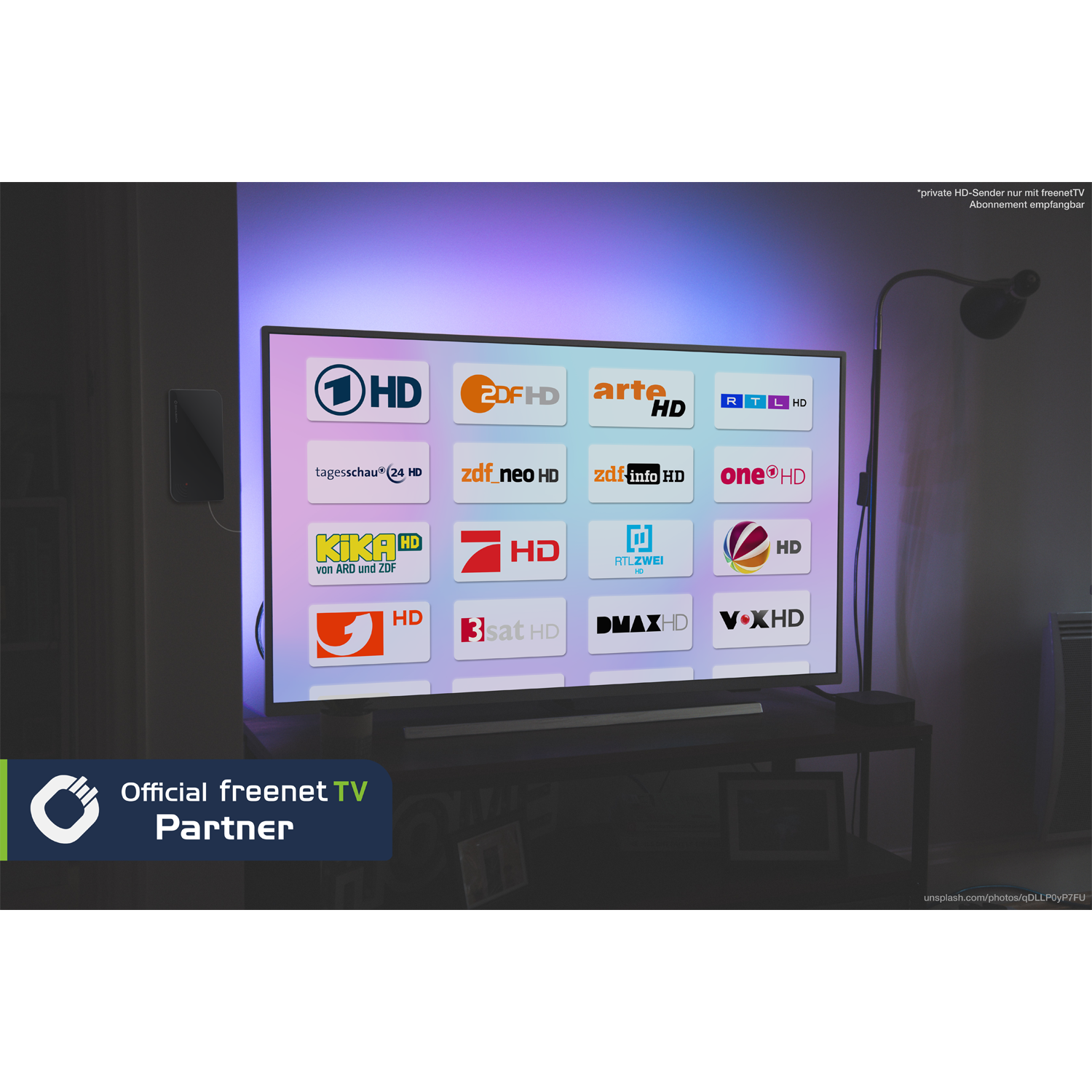 Ein Fernsehbildschirm zeigt verschiedene HD-Senderlogos. Die Szene umfasst einen dunklen Tisch, eine Lampe und ein 'freenet TV'-Partnerlogo.
