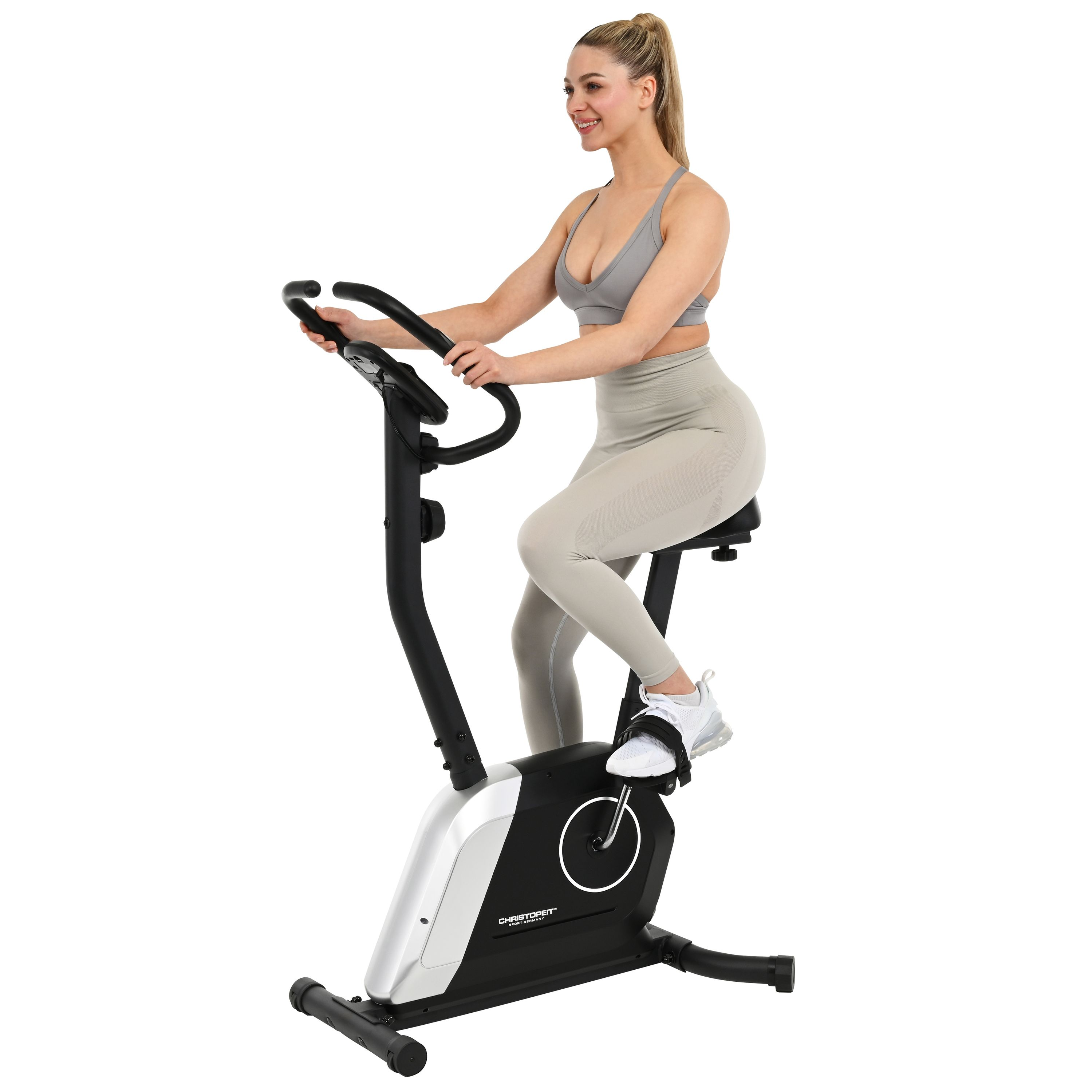 Eine Frau in Sportkleidung trainiert auf einem Heimtrainer und lächelt. Das Fahrrad ist schwarz und silber.