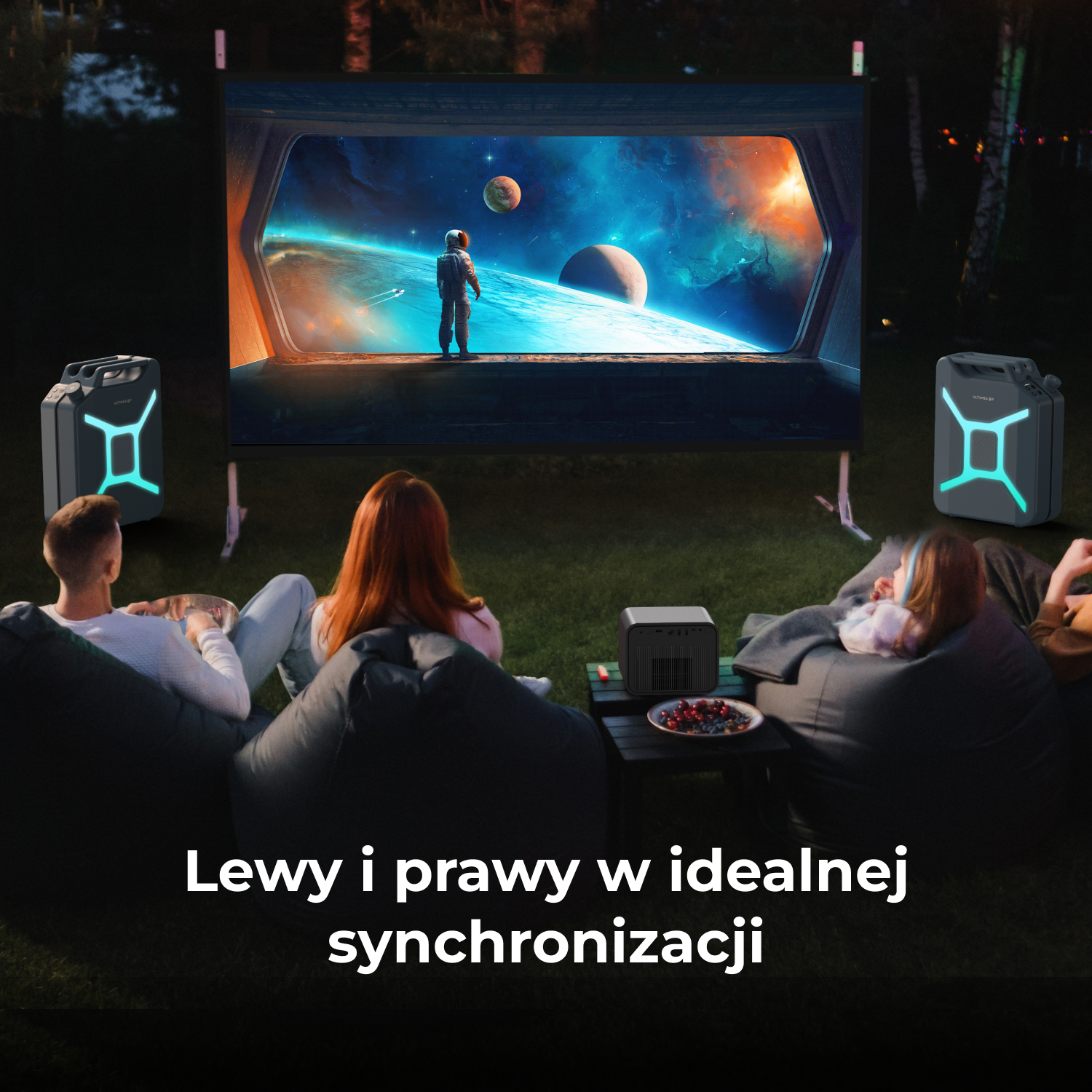 Ludzie oglądają film wyświetlany na ekranie na zewnątrz. Film pokazuje astronautę na planecie. Głośniki flankują ekran.