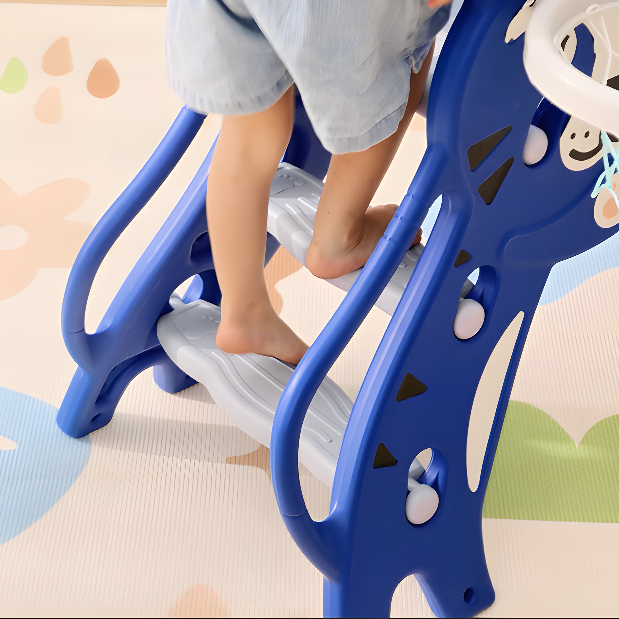 Un bambino sale su una struttura di gioco blu e bianca. La struttura è su un pavimento fantasia dai colori chiari.