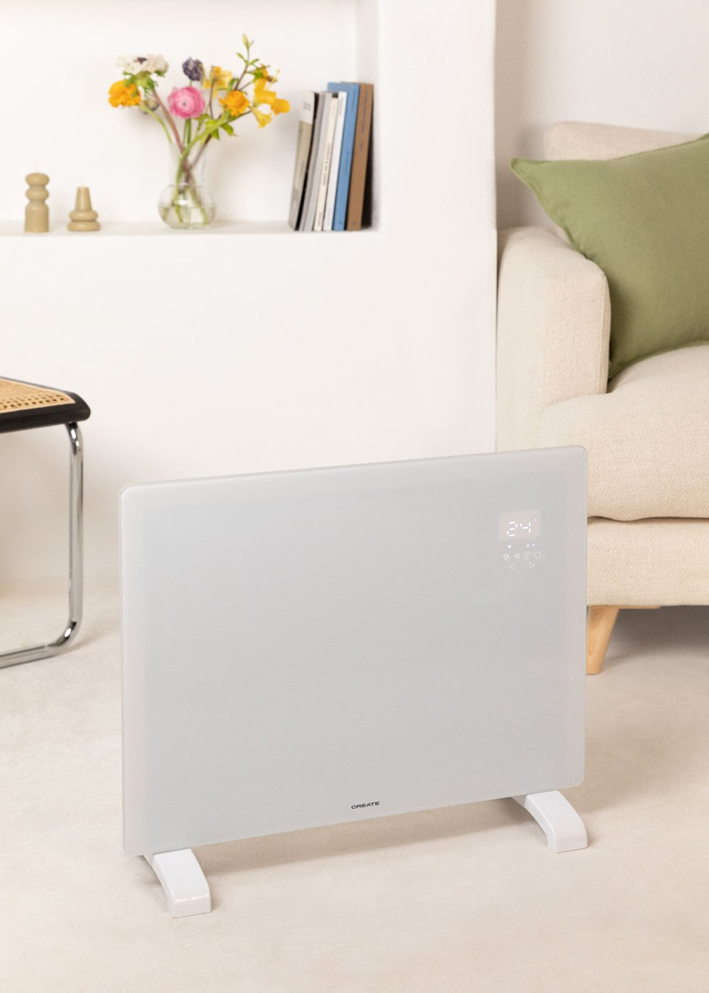 Un calefactor eléctrico blanco en primer plano. En el fondo se ven un sofá, flores en un jarrón y libros.