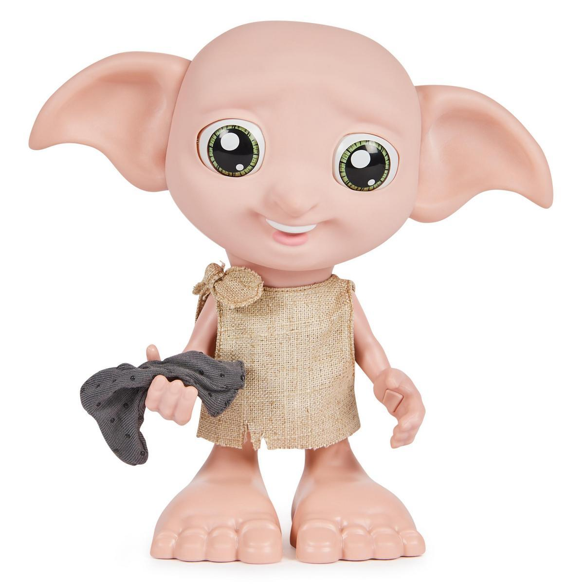 Una muñeca Dobby con grandes ojos verdes, orejas grandes y un atuendo de saco de arpillera, sosteniendo un calcetín gris. El fondo es blanco.