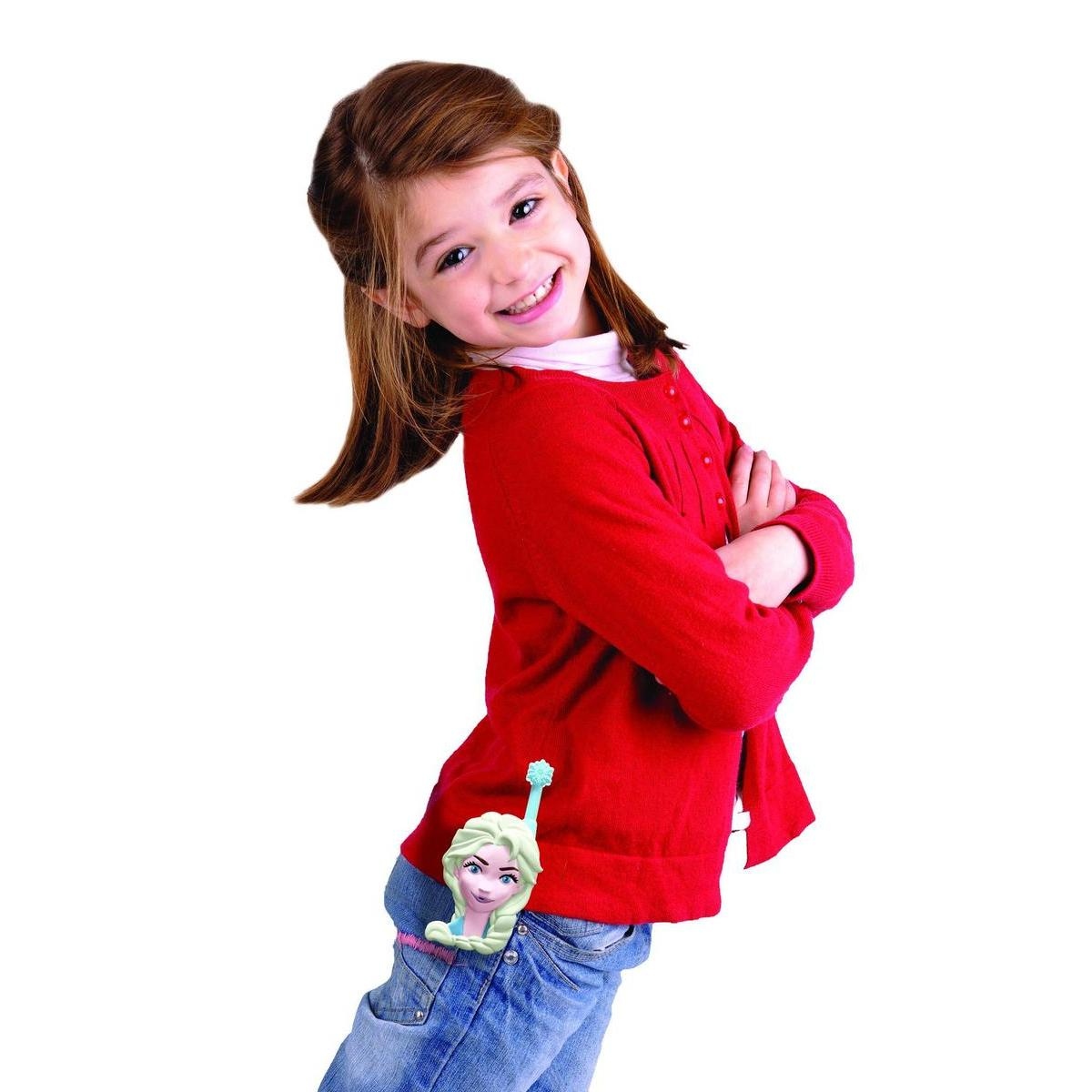 Una niña sonriente con un suéter rojo y jeans tiene los brazos cruzados. Un juguete de Elsa está sujeto a sus jeans.