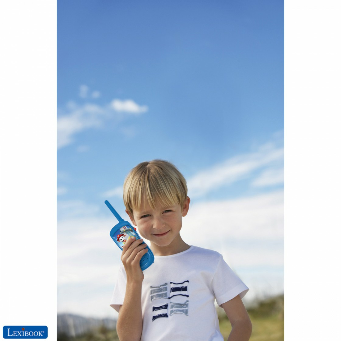 Ein Junge hält ein blaues Walkie-Talkie unter blauem Himmel. Er trägt ein weißes Hemd. Das Walkie-Talkie hat einen Paw Patrol-Charakter.