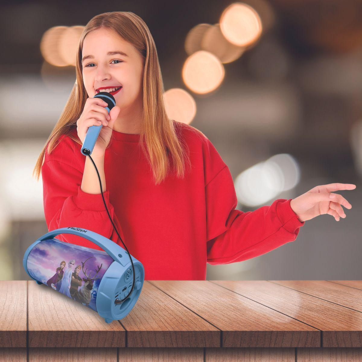 Una niña canta en un micrófono azul. Un altavoz azul con personajes de Frozen está sobre una mesa.