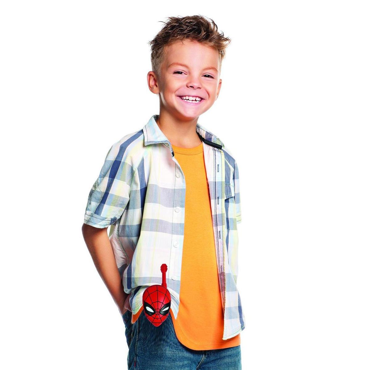 Un niño sonriente usa una camisa a cuadros sobre una camiseta naranja. Un juguete de Spider-Man está en su bolsillo.