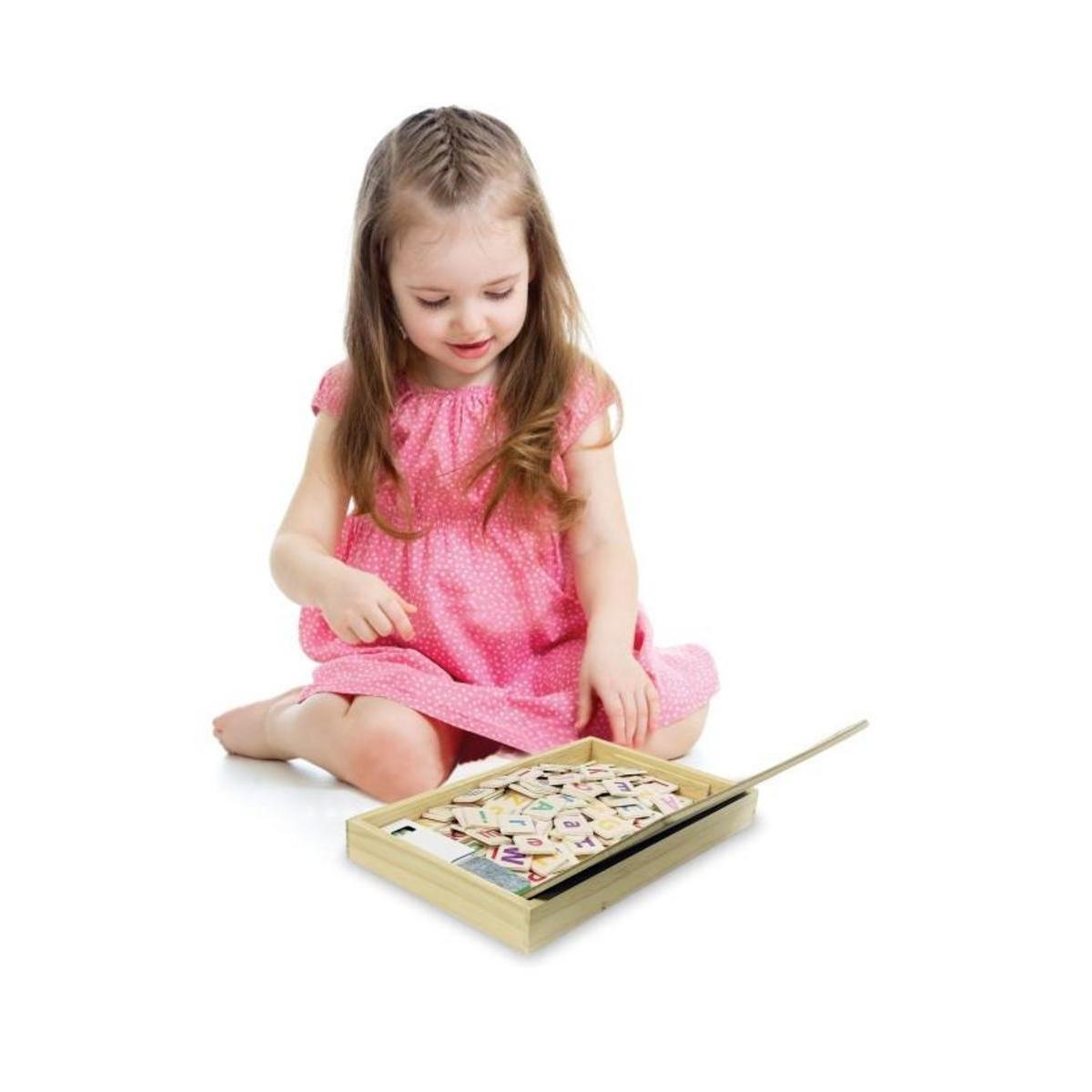 Una niña con un vestido rosa está sentada en el suelo, mirando bloques de letras en una caja de madera.