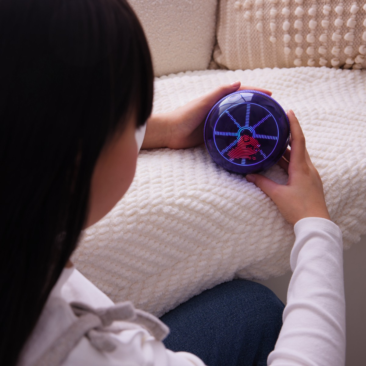 Una persona tiene in mano un dispositivo viola luminoso. Il dispositivo mostra una grafica rossa e blu. La persona è seduta su una coperta bianca.