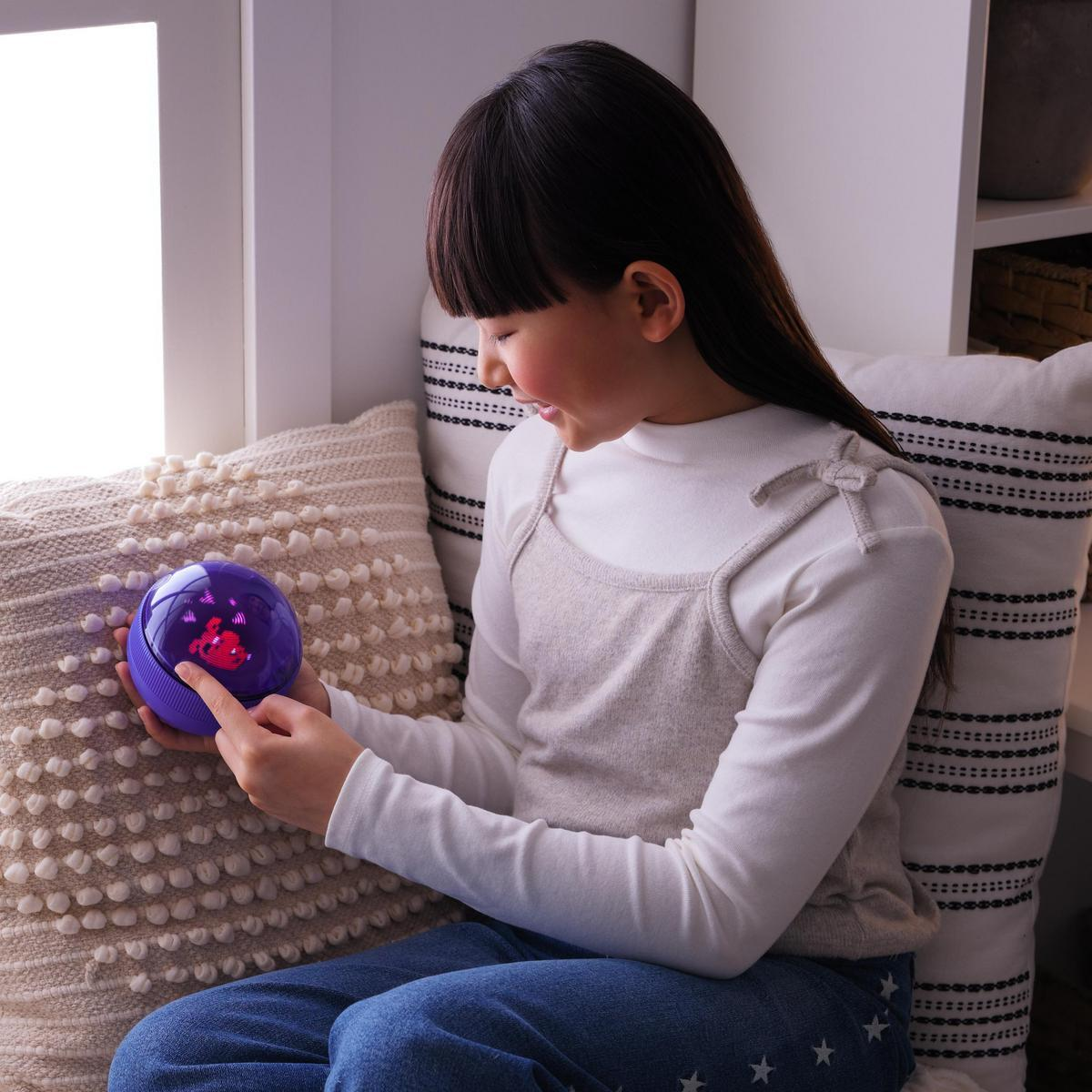 Una ragazza indica un globo viola. Il globo mostra una figura rossa. È seduta vicino a una finestra con cuscini.