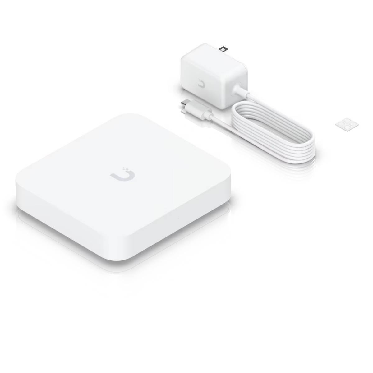 Białe kwadratowe urządzenie, zasilacz z kablem i mały biały kwadrat na białej powierzchni.