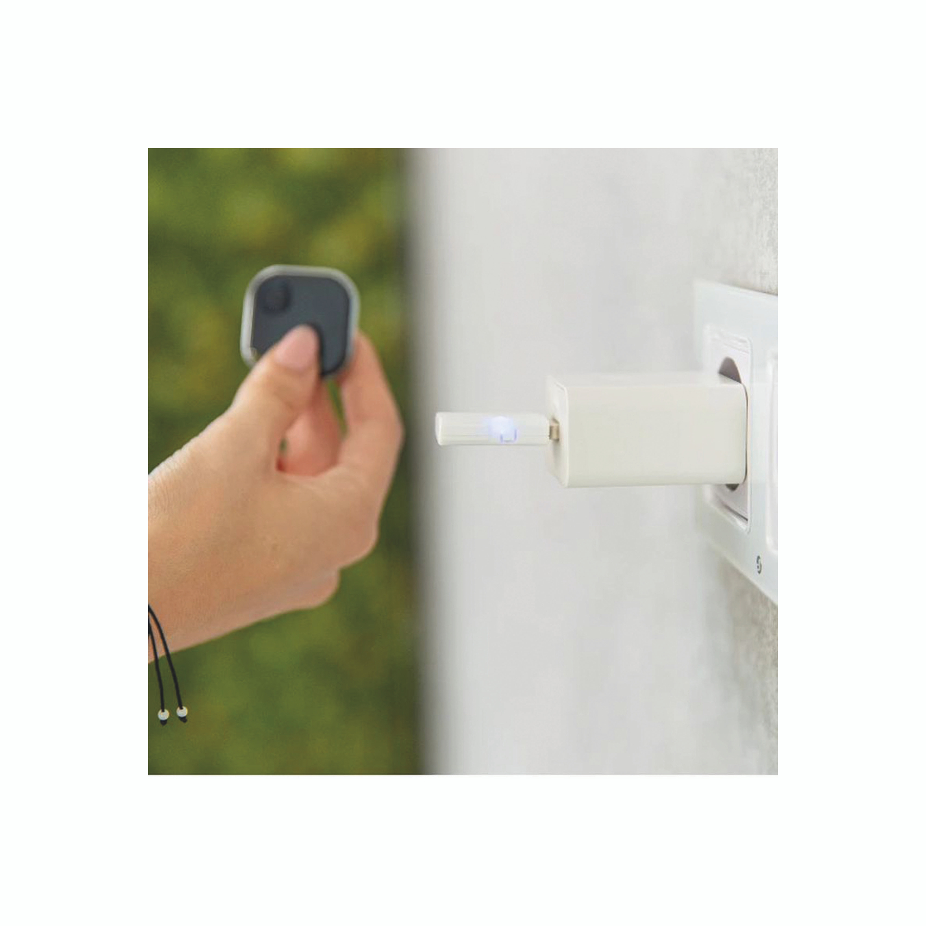 Une main tient un appareil carré noir. Un chargeur blanc est dans une prise murale. Fond vert.