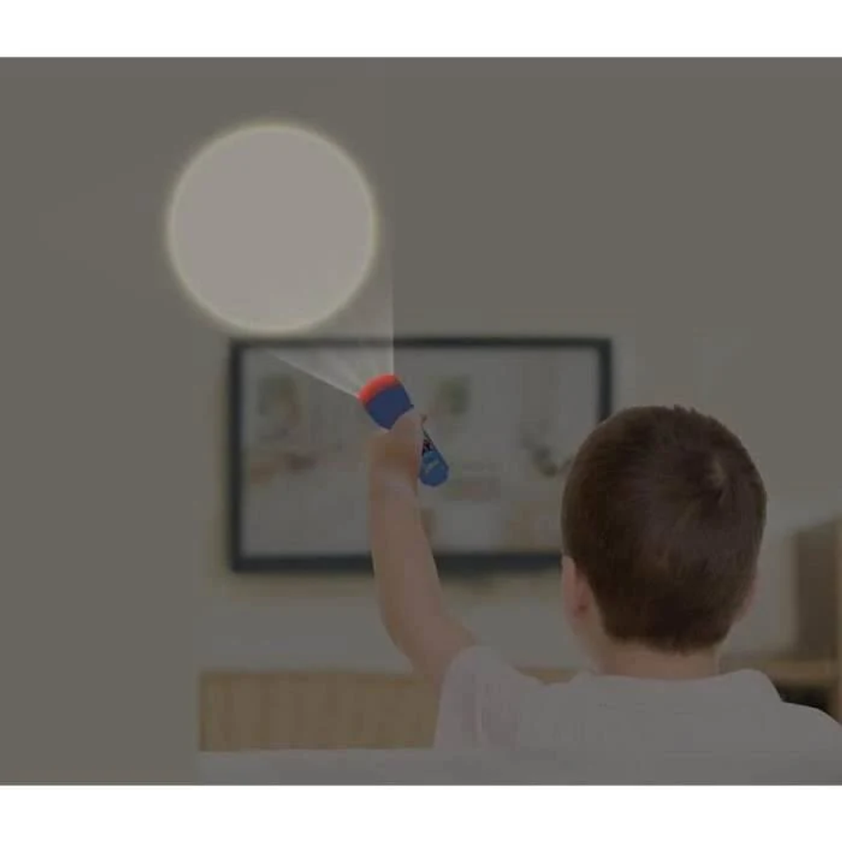 Un niño sostiene una linterna azul proyectando un círculo de luz en la pared. Un cuadro cuelga al fondo.