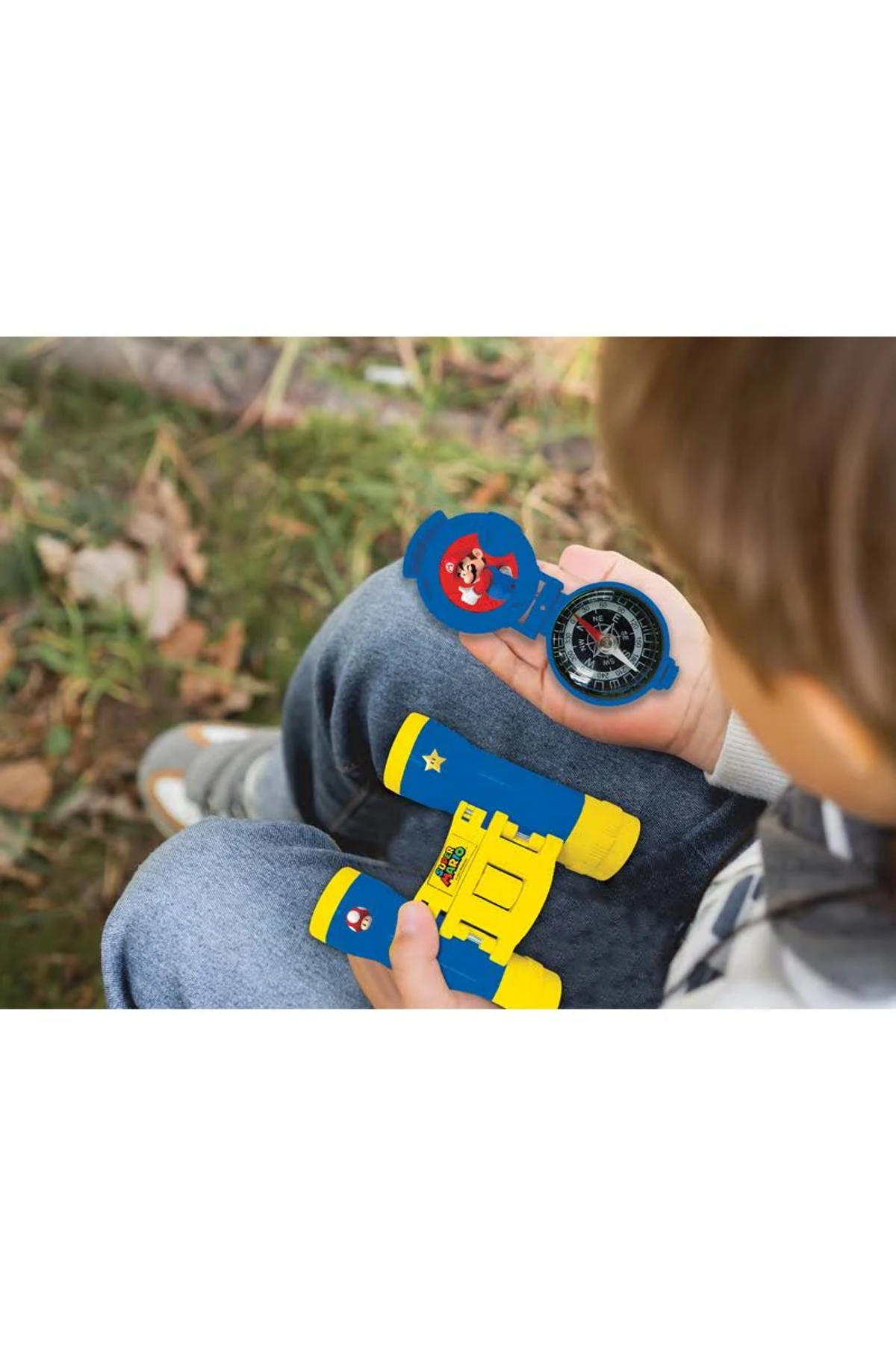 Ein Kind hält einen blauen Kompass und ein Spielzeugteleskop mit gelben Akzenten, mit Super Mario-Figuren, im Freien.