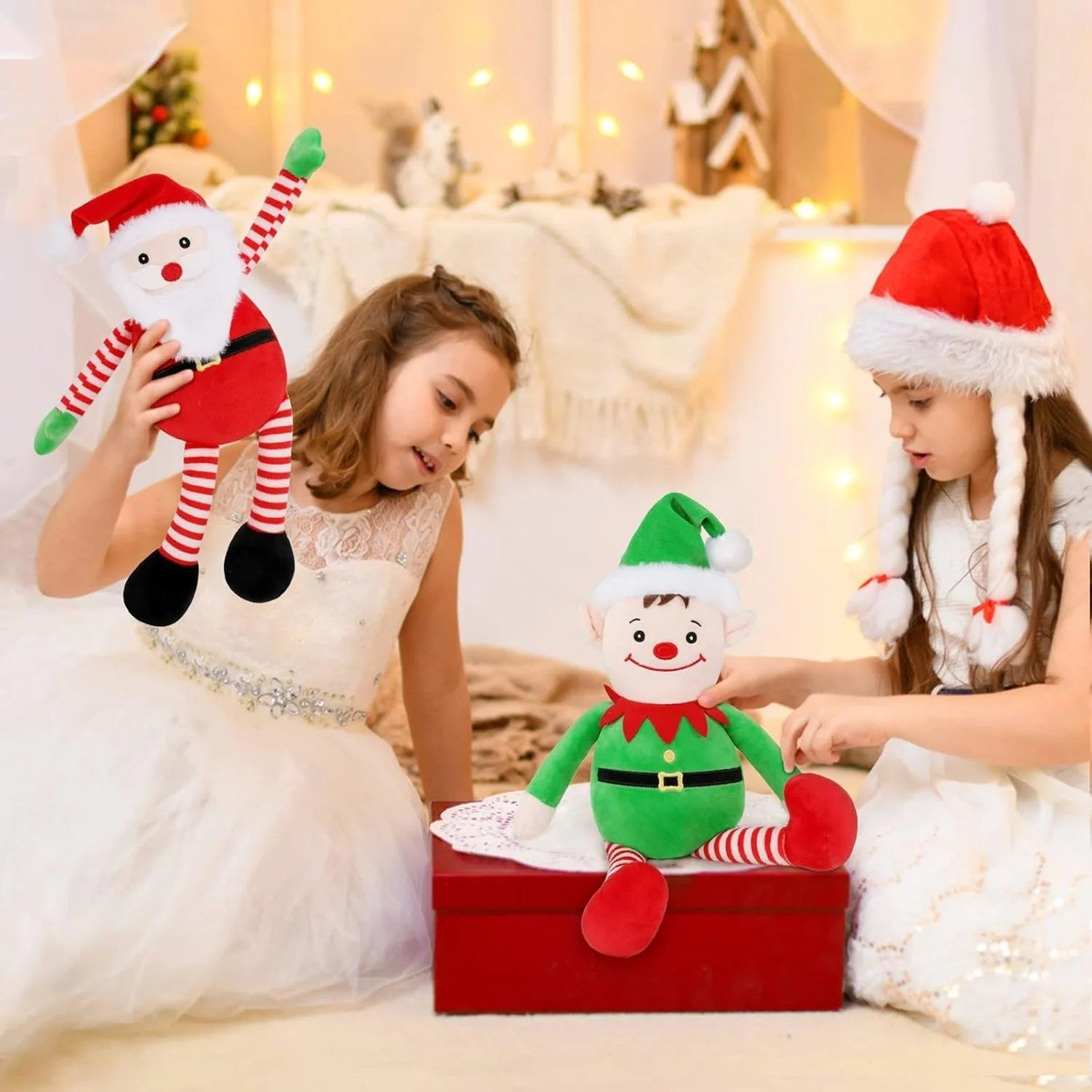 Due ragazze con giocattoli natalizi. Una tiene in mano una bambola di Babbo Natale, l'altra una bambola di elfo. Entrambe indossano abiti bianchi e cappelli natalizi.