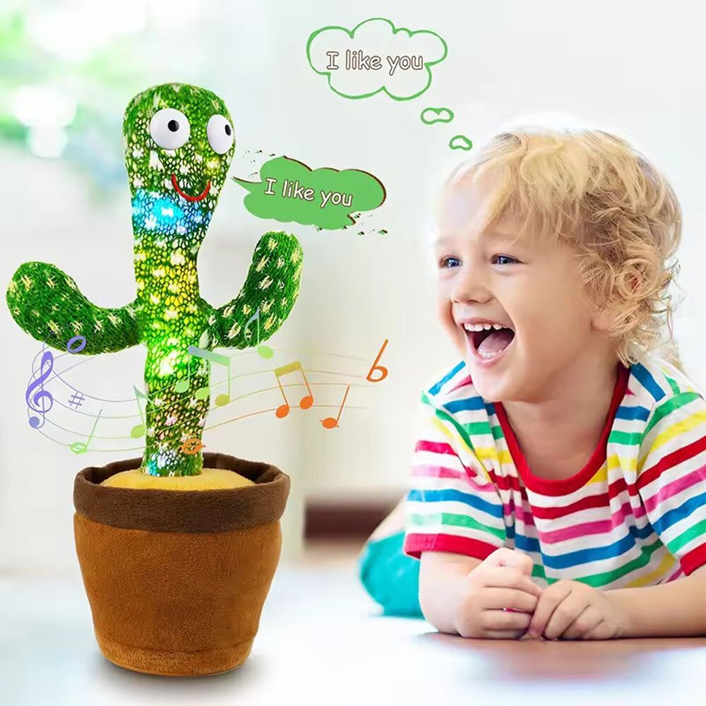 Un niño se ríe de un juguete de cactus. El juguete dice "Me gustas" y reproduce música. El cactus es verde y está en una maceta marrón.