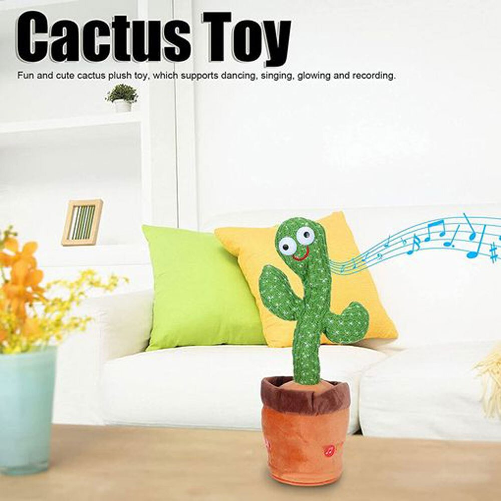 Un juguete de cactus en una maceta está sobre una mesa. Es verde con una cara sonriente. Hay almohadas y un sofá detrás.