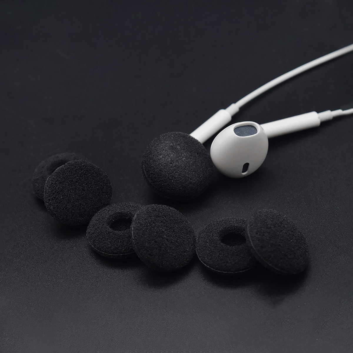 Białe słuchawki z czarnymi piankowymi osłonami i zapasowymi osłonami na czarnej powierzchni.