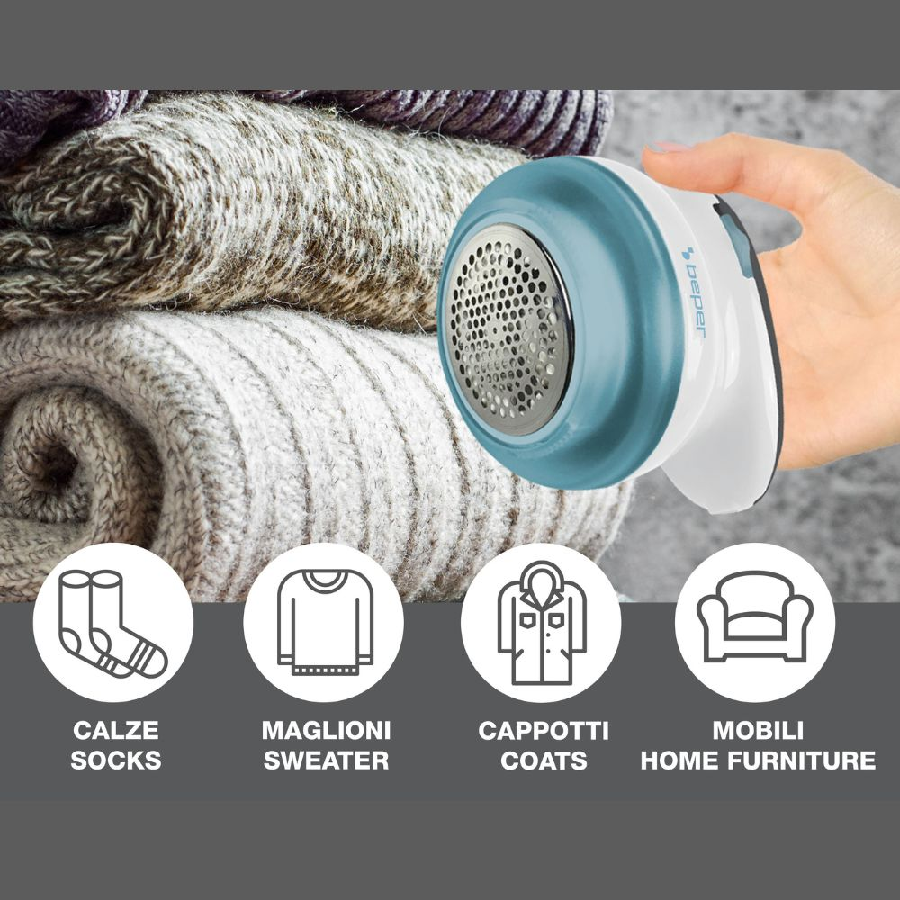 Una mano tiene un rasoio per tessuti blu e bianco. Sullo sfondo maglioni piegati impilati, con icone di vestiti davanti.