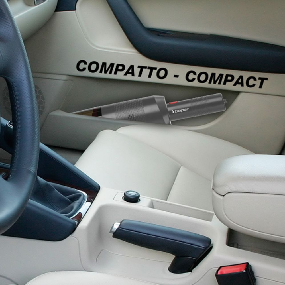 Interni auto con aspirapolvere compatto, etichettato 'COMPATTO-COMPACT'. I sedili sono beige, il cruscotto scuro.