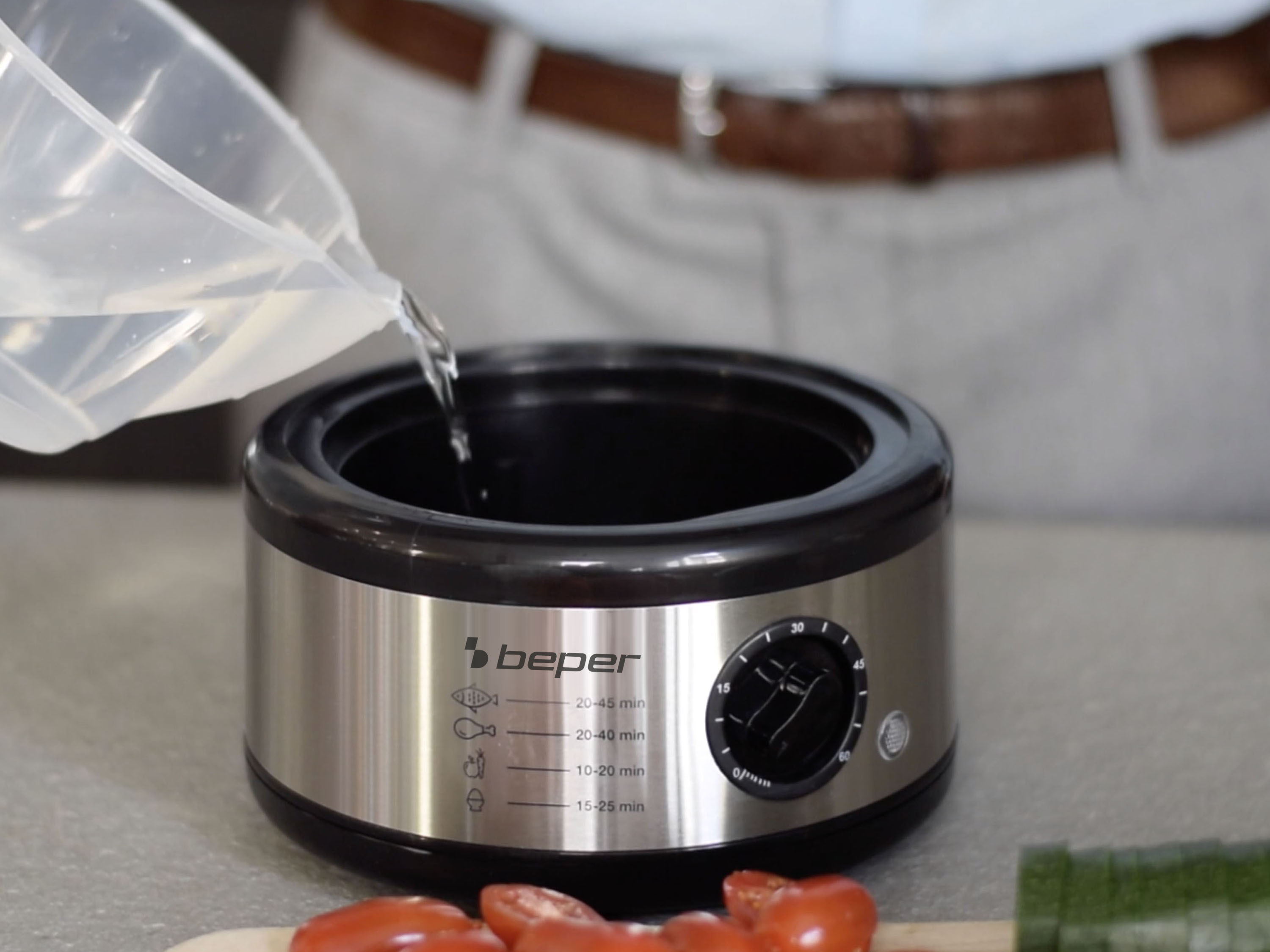 Una persona versa acqua in una slow cooker argento e nera, con timer e il marchio 'beper'.