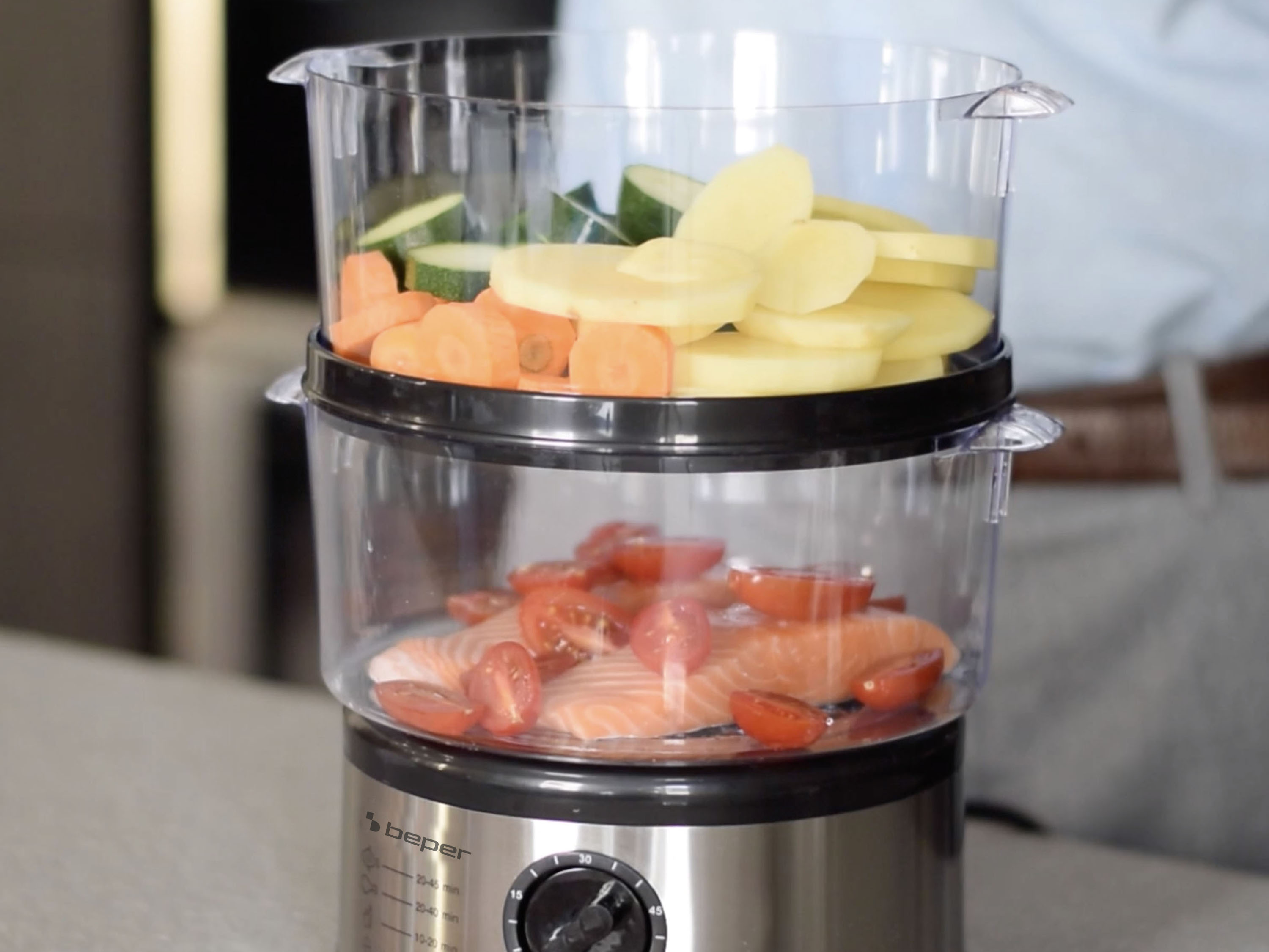 Una vaporiera con verdure e pesce. Strato superiore: carote, zucchine, patate. Strato inferiore: salmone e pomodori.