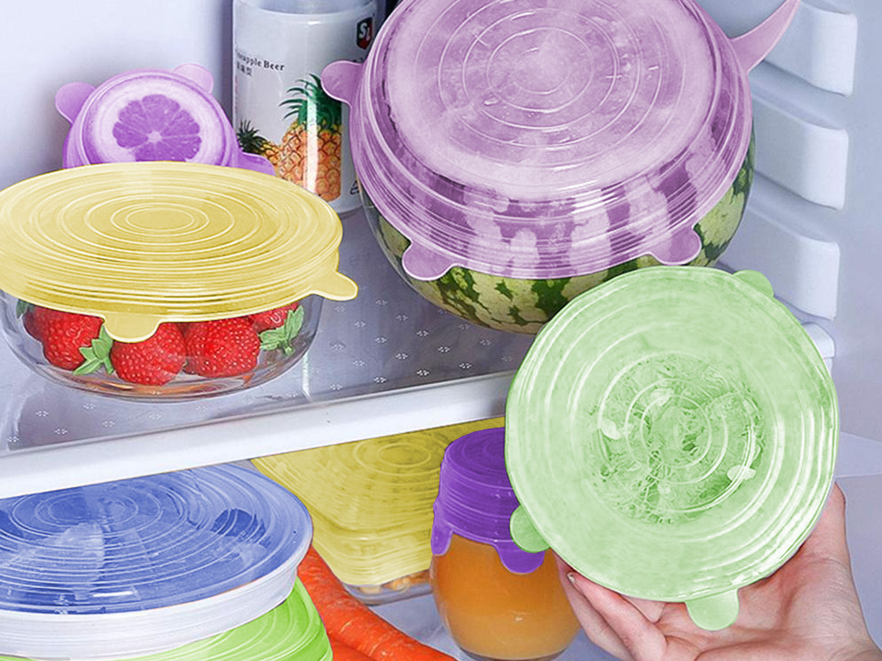 Un frigorifero con cibo coperto da coperchi in silicone colorati. Include fragole, anguria e vasetti.