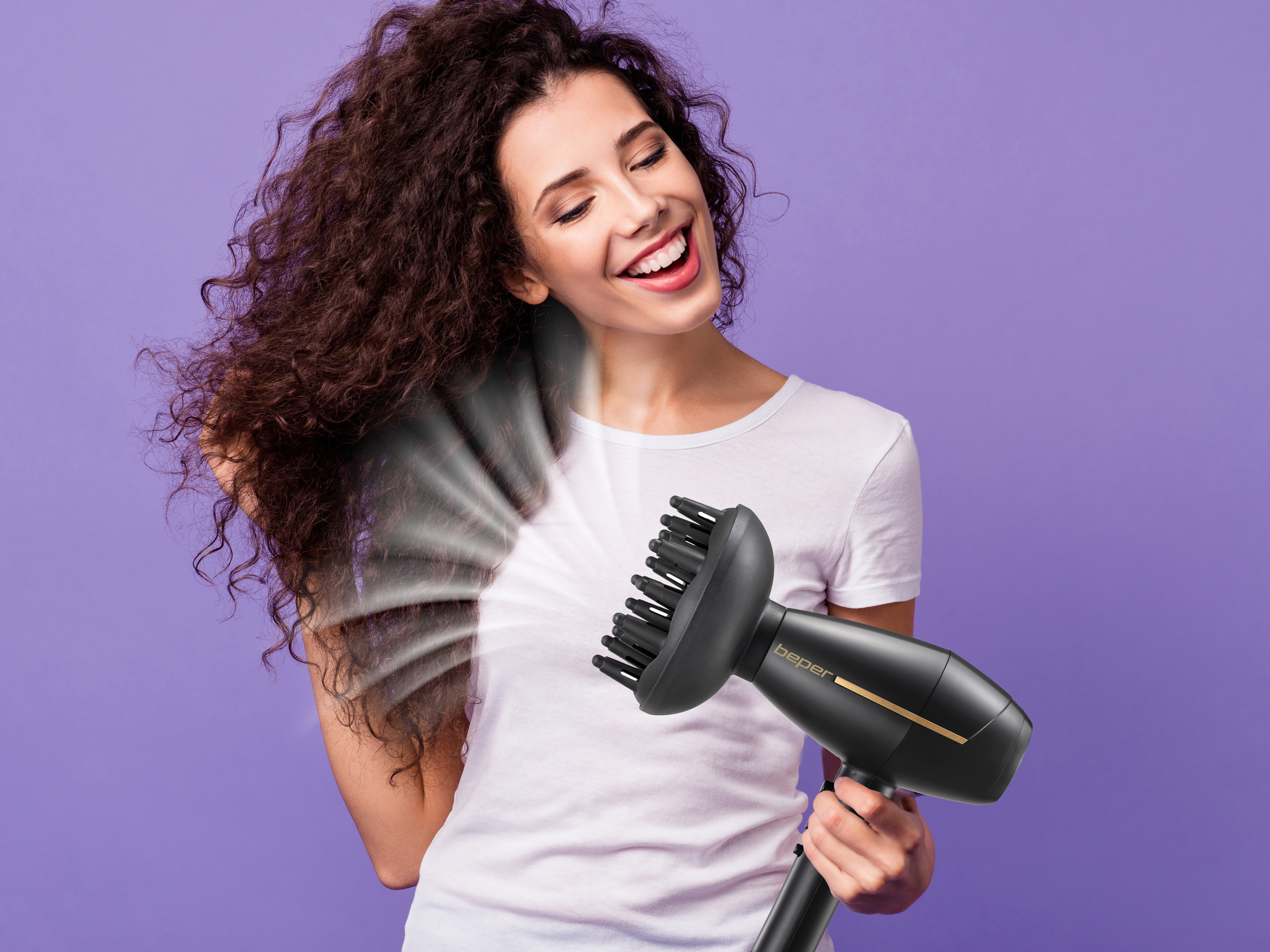 Donna sorride, usa un asciugacapelli nero sui suoi capelli ricci. Sfondo viola.