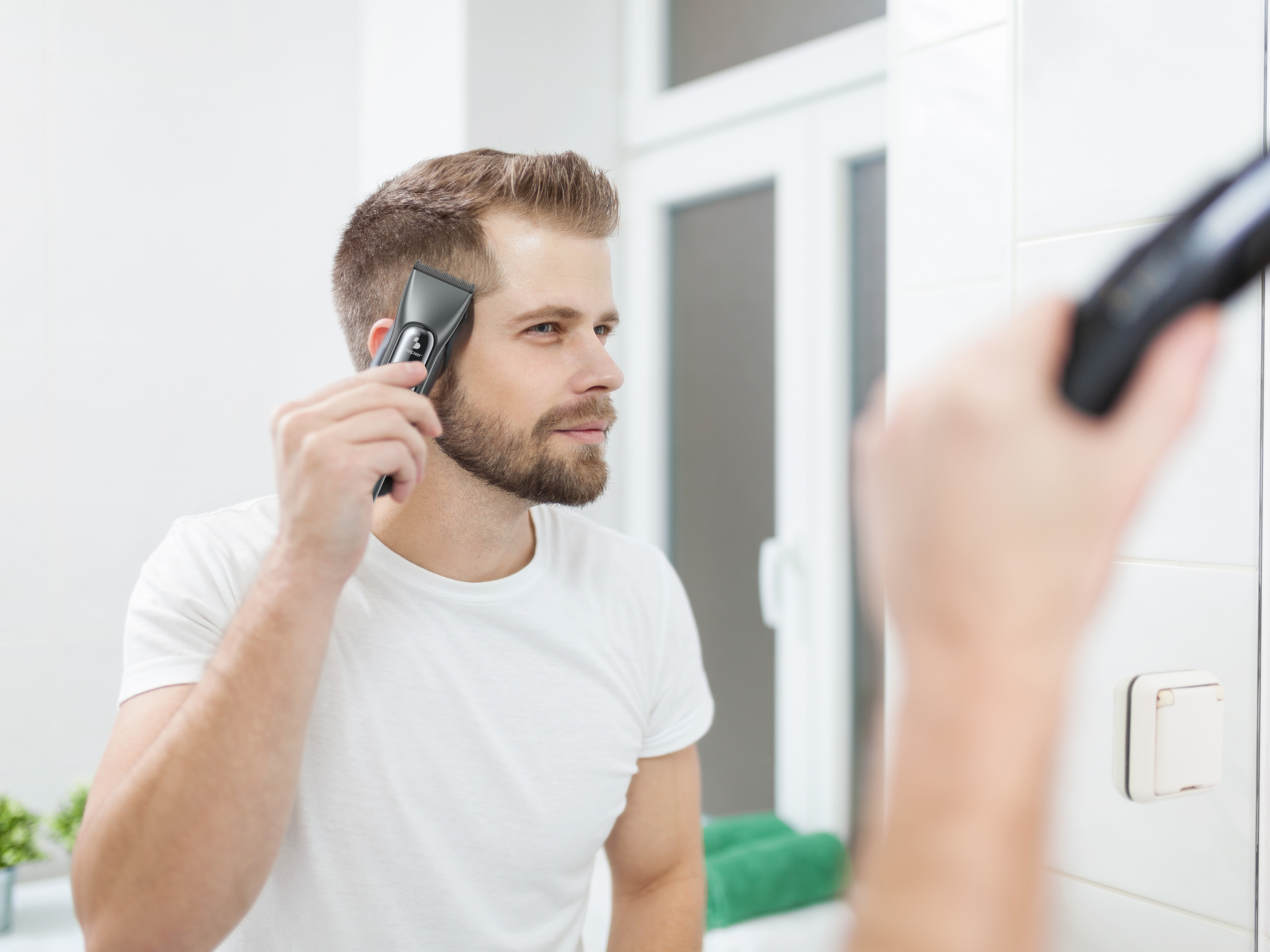 Un uomo si rade i capelli in bagno, usando un rasoio elettrico davanti a uno specchio.