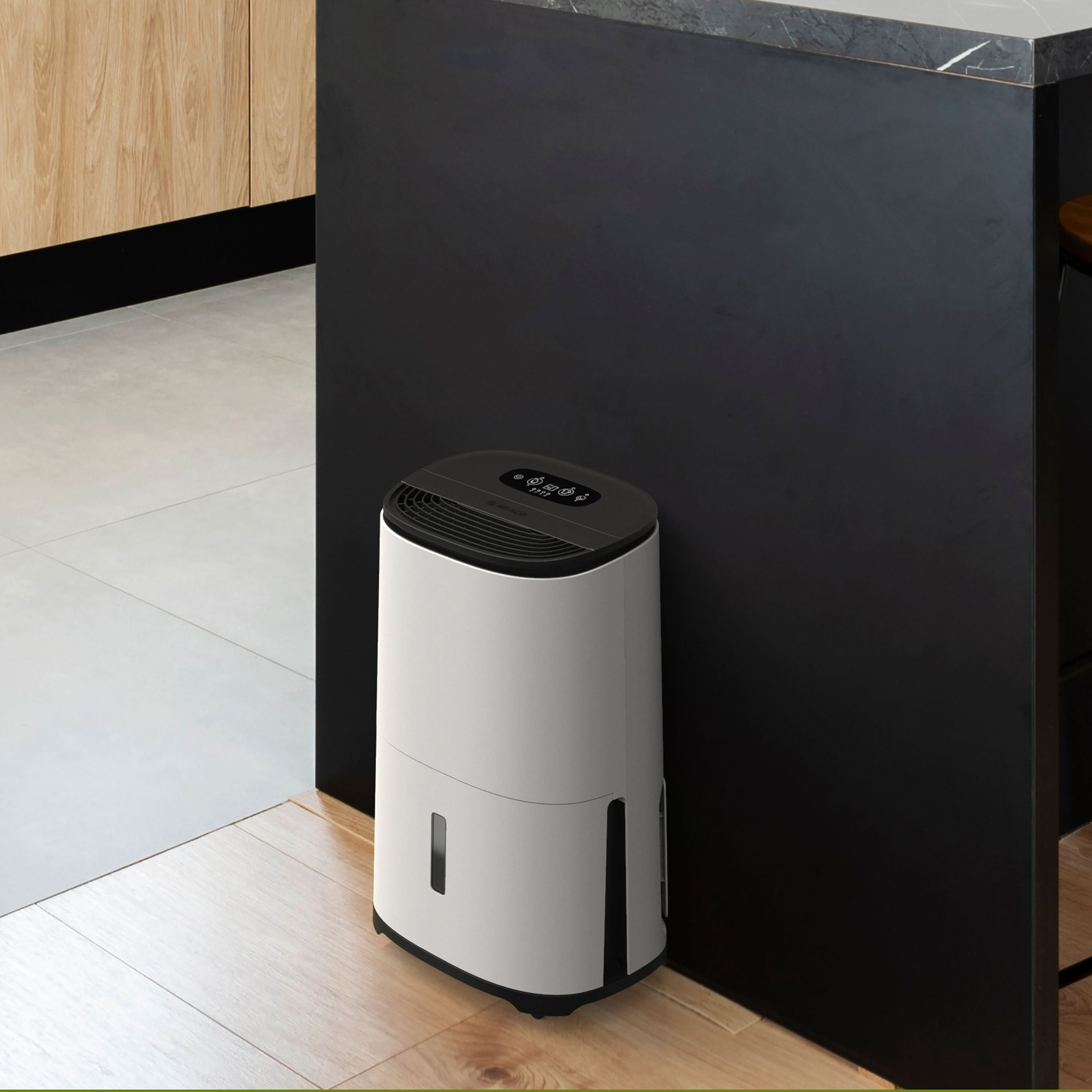 Biały i czarny osuszacz stoi na drewnianej podłodze. Czarny blat i szafki w tle.