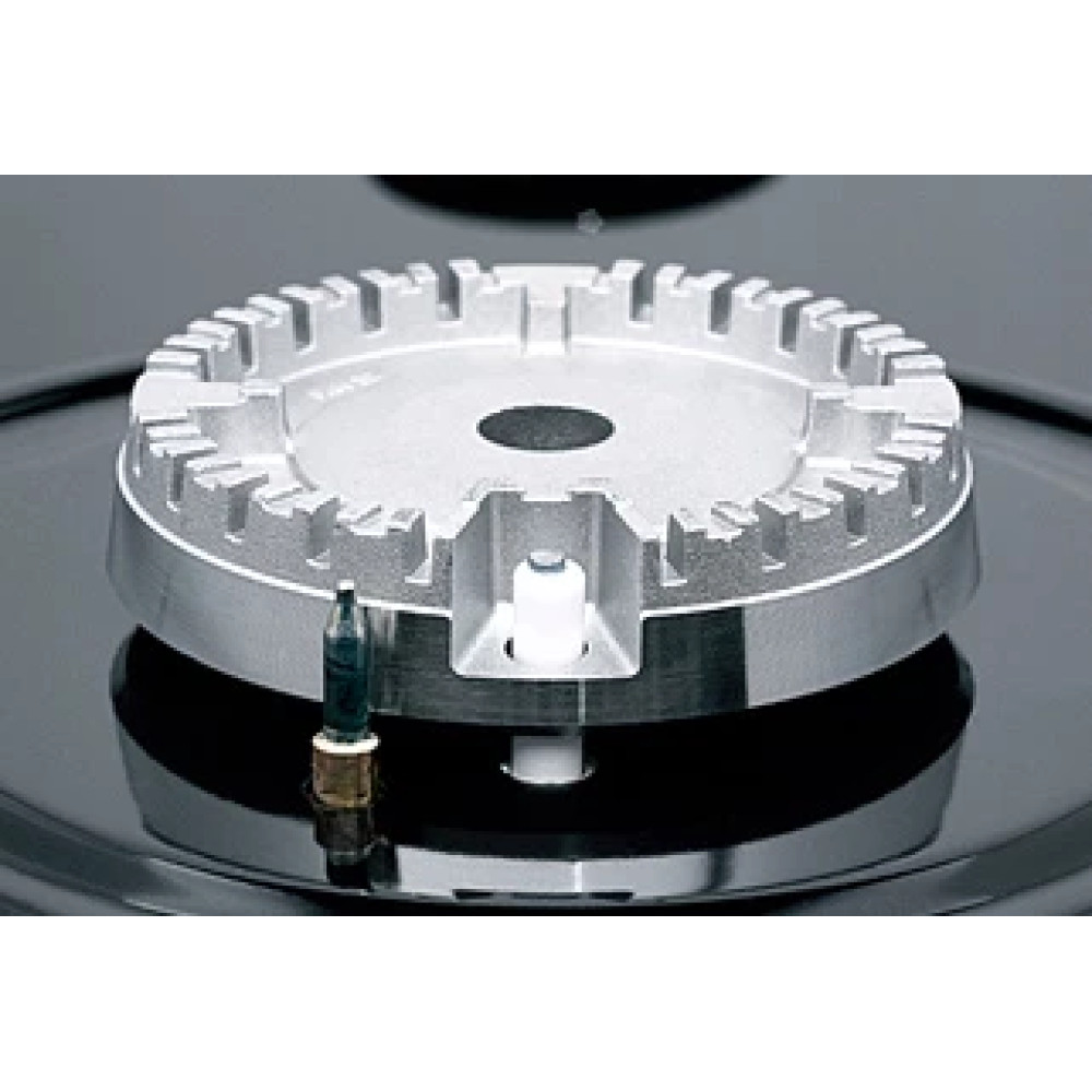 Zbliżenie palnika kuchenki gazowej. Palnik jest srebrny z czarnym blatem kuchenki. Obok palnika znajduje się mała świeca zapłonowa.