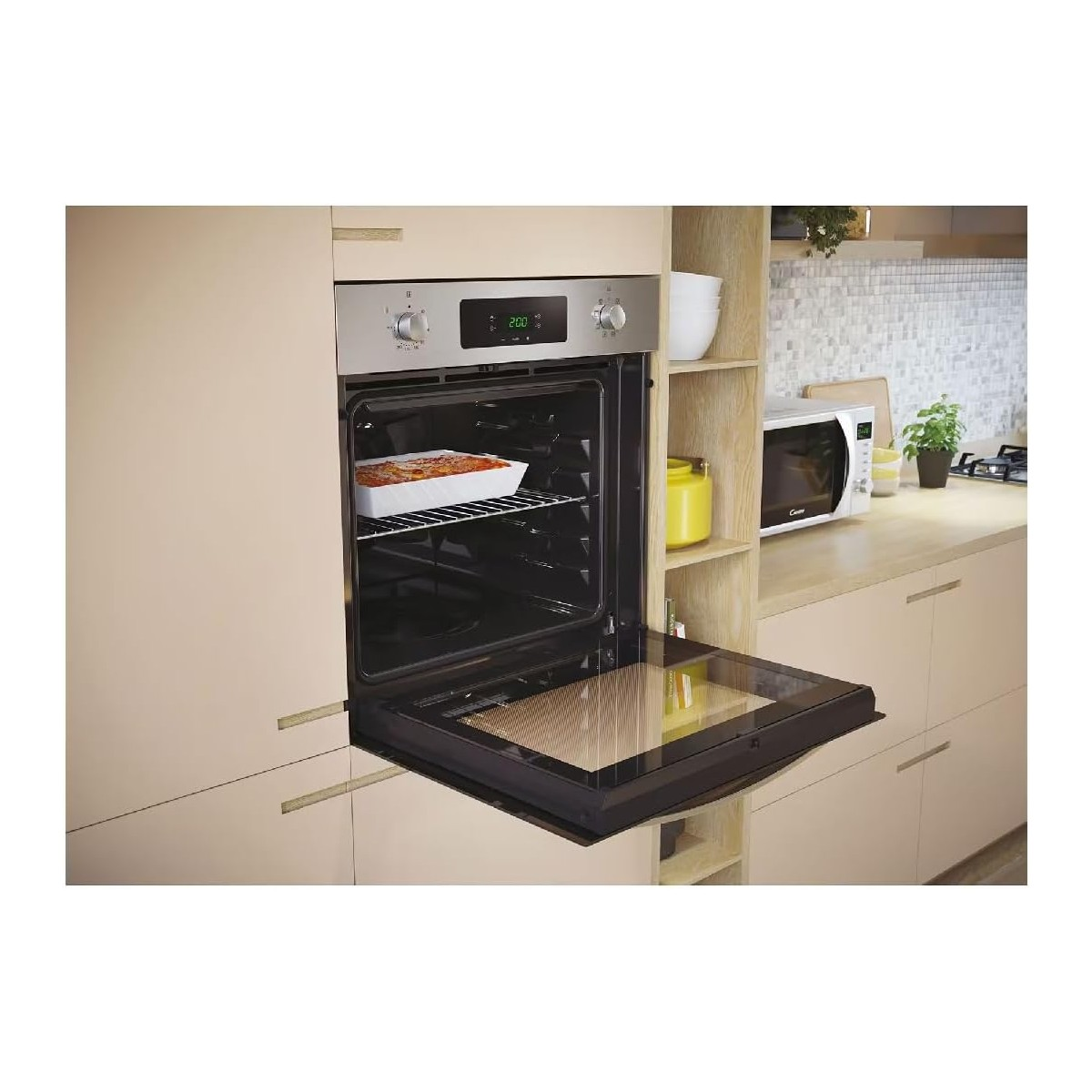 Un forno con la porta aperta, un piatto all'interno. Nel retro si vedono un microonde e altri articoli da cucina.