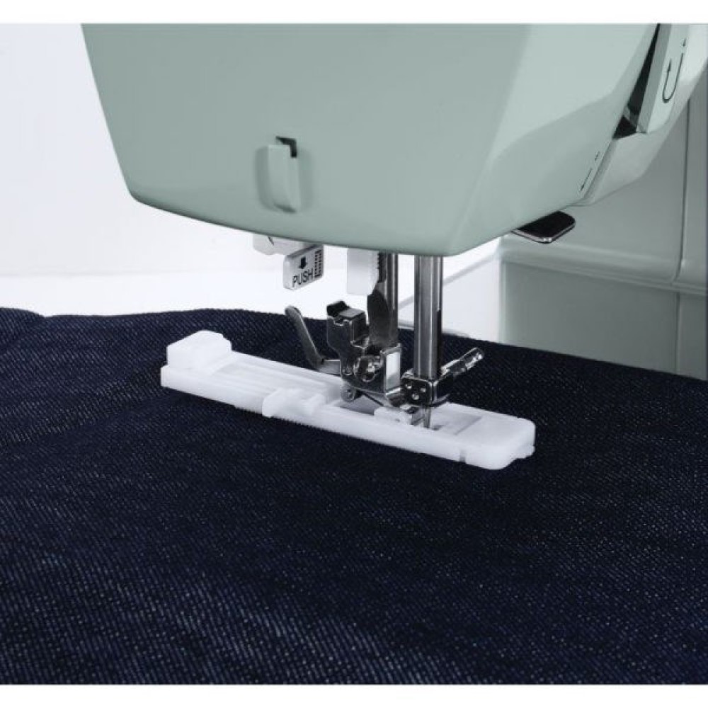 Stopka dociskowa maszyny do szycia na ciemnym dżinsie. Maszyna jest jasnozielona, stopka biała. Zbliżenie.