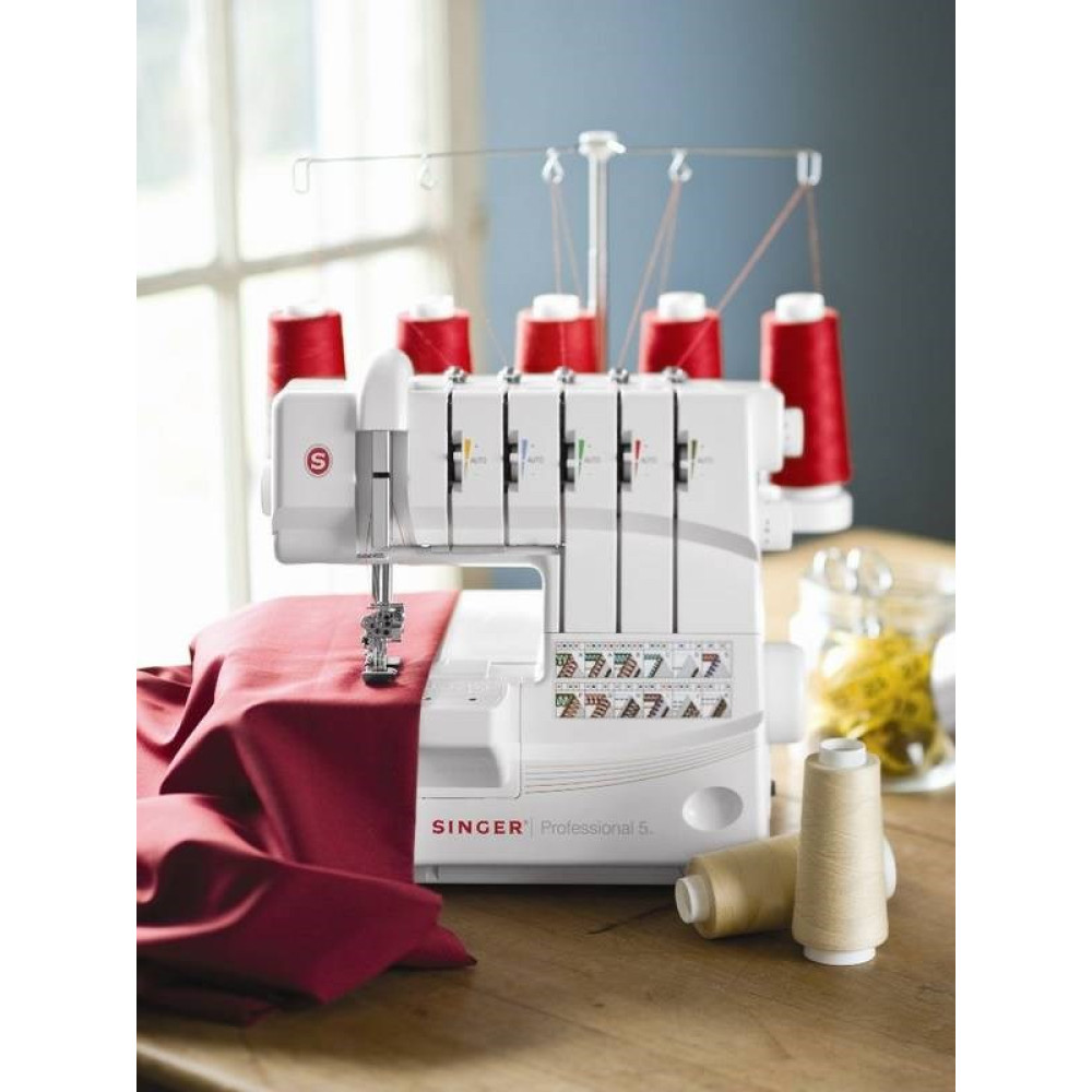 Biała maszyna do szycia Singer z czerwonymi szpulkami nici. Czerwona tkanina pod igłą. Tło: drewniany stół i okno.