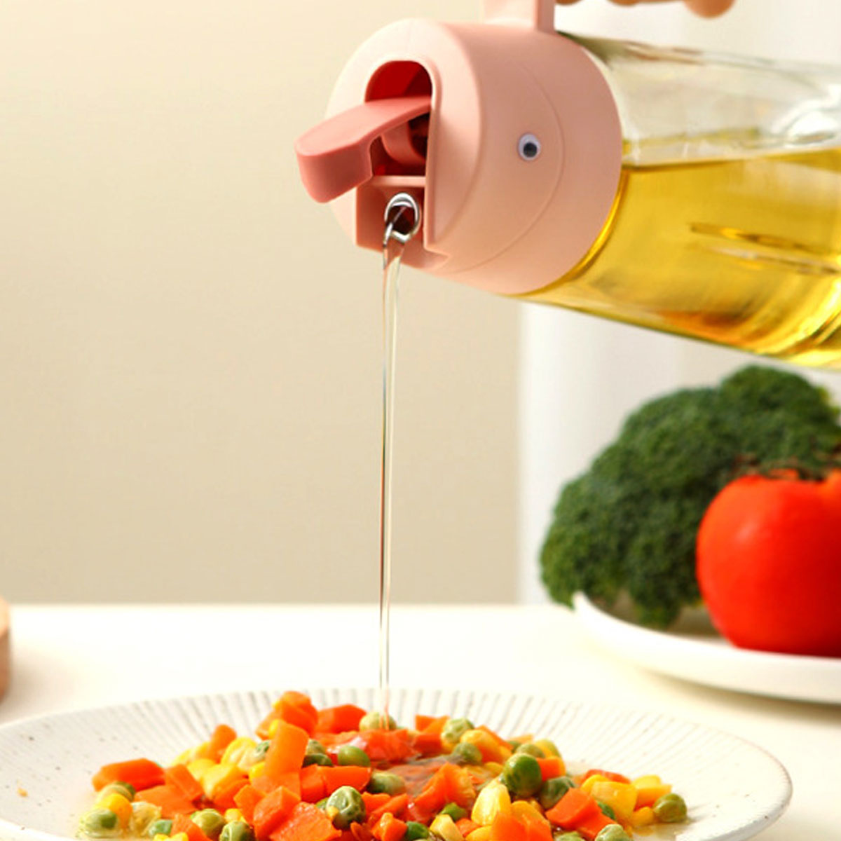 Öl gießt aus einem Spender auf einen Teller mit Gemüse. Im Hintergrund sind Brokkoli und eine Tomate.