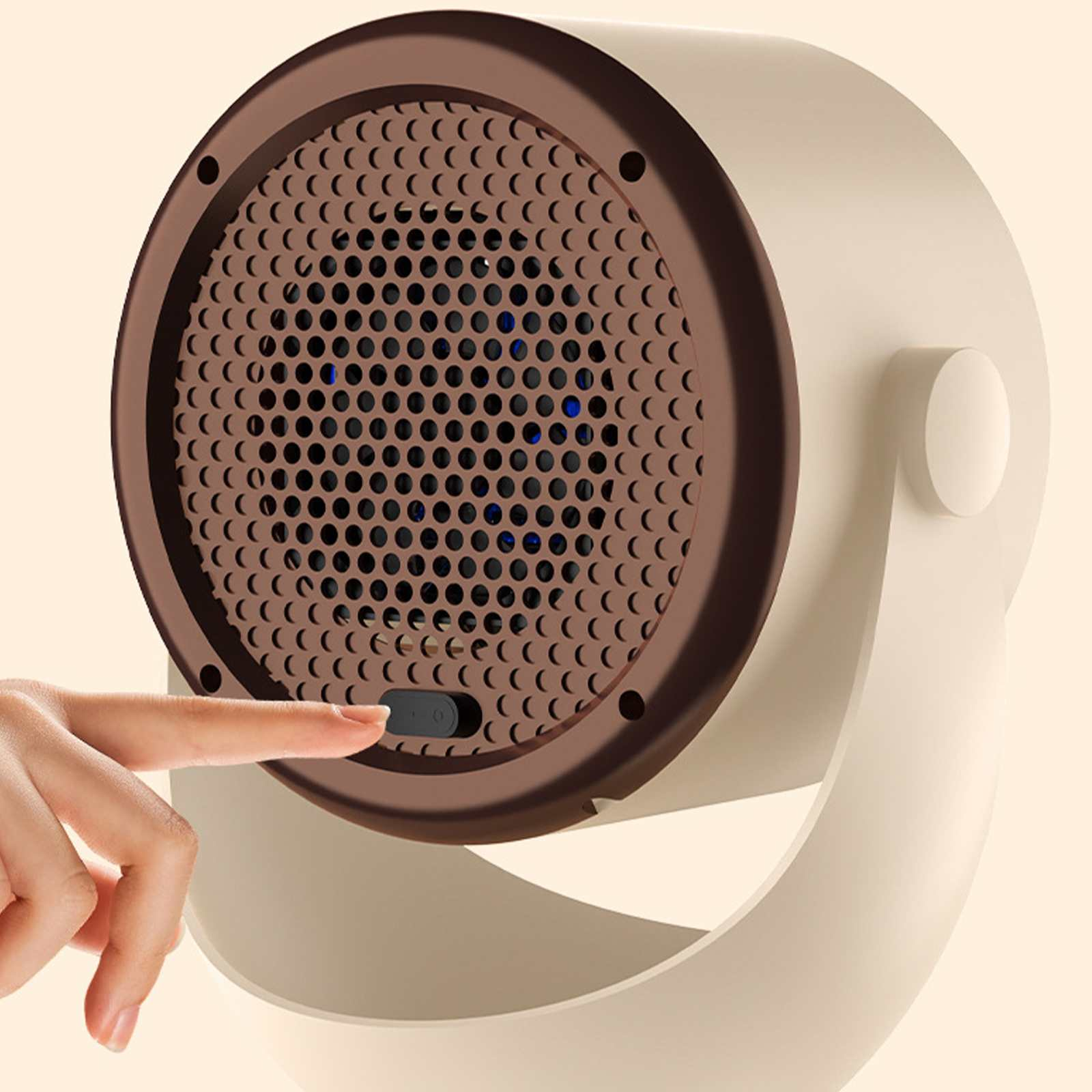 Ein beige-brauner elektrischer Heizlüfter. Ein Finger drückt den Einschaltknopf. Der Hintergrund ist cremefarben.