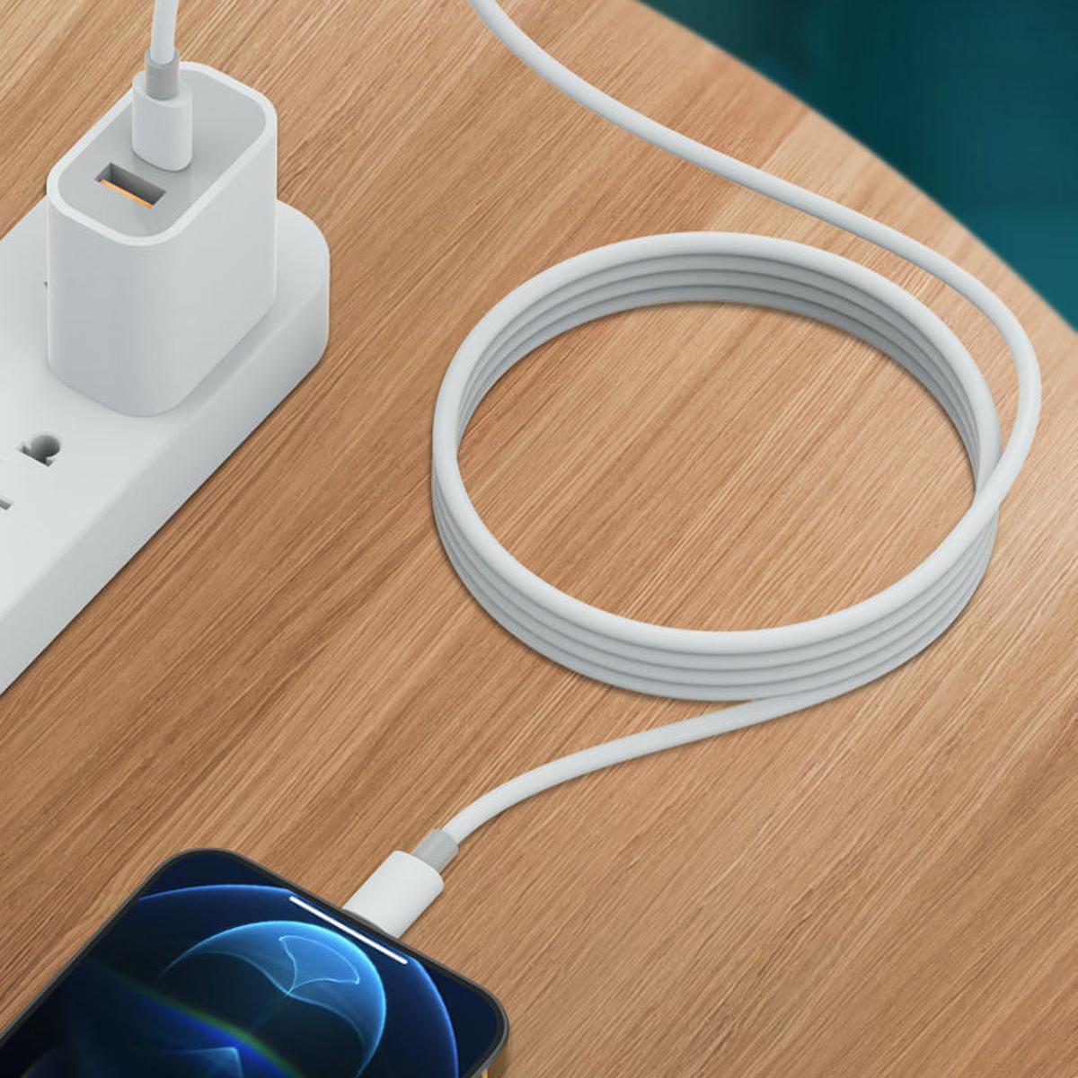 Ein Telefon, das mit einem weißen Kabel geladen wird, das mit einem Netzteil und einer Steckdose verbunden ist. Der Hintergrund ist ein Holztisch.