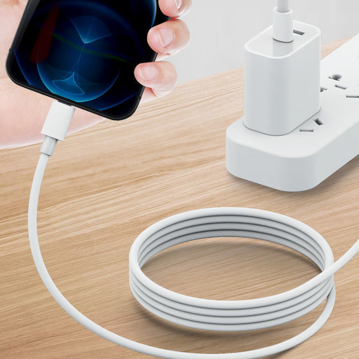 Eine Hand hält ein Telefon, das mit einem weißen Ladekabel verbunden ist. Das Kabel führt zu einem Netzteil auf einer Holzoberfläche.
