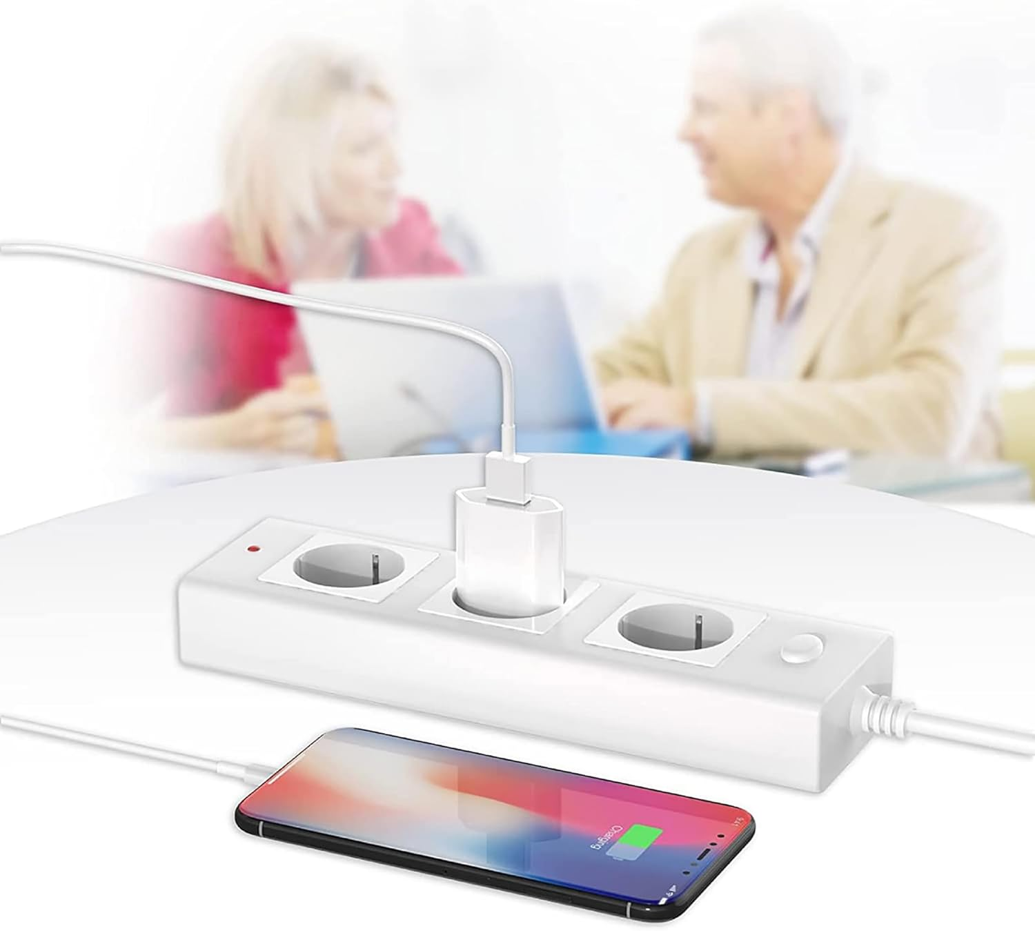 Ein Telefon wird geladen. Eine weiße Steckdosenleiste mit Ladegerät und zwei Personen im Hintergrund unscharf.