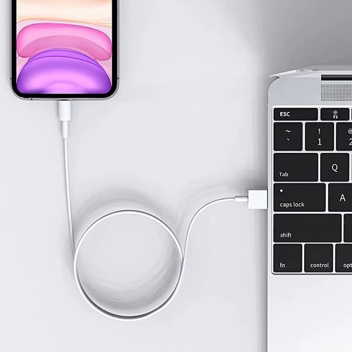 Ein Telefon, das mit einem weißen Kabel an einem Laptop aufgeladen wird. Das Telefon zeigt ein lila-weißes Bild an.