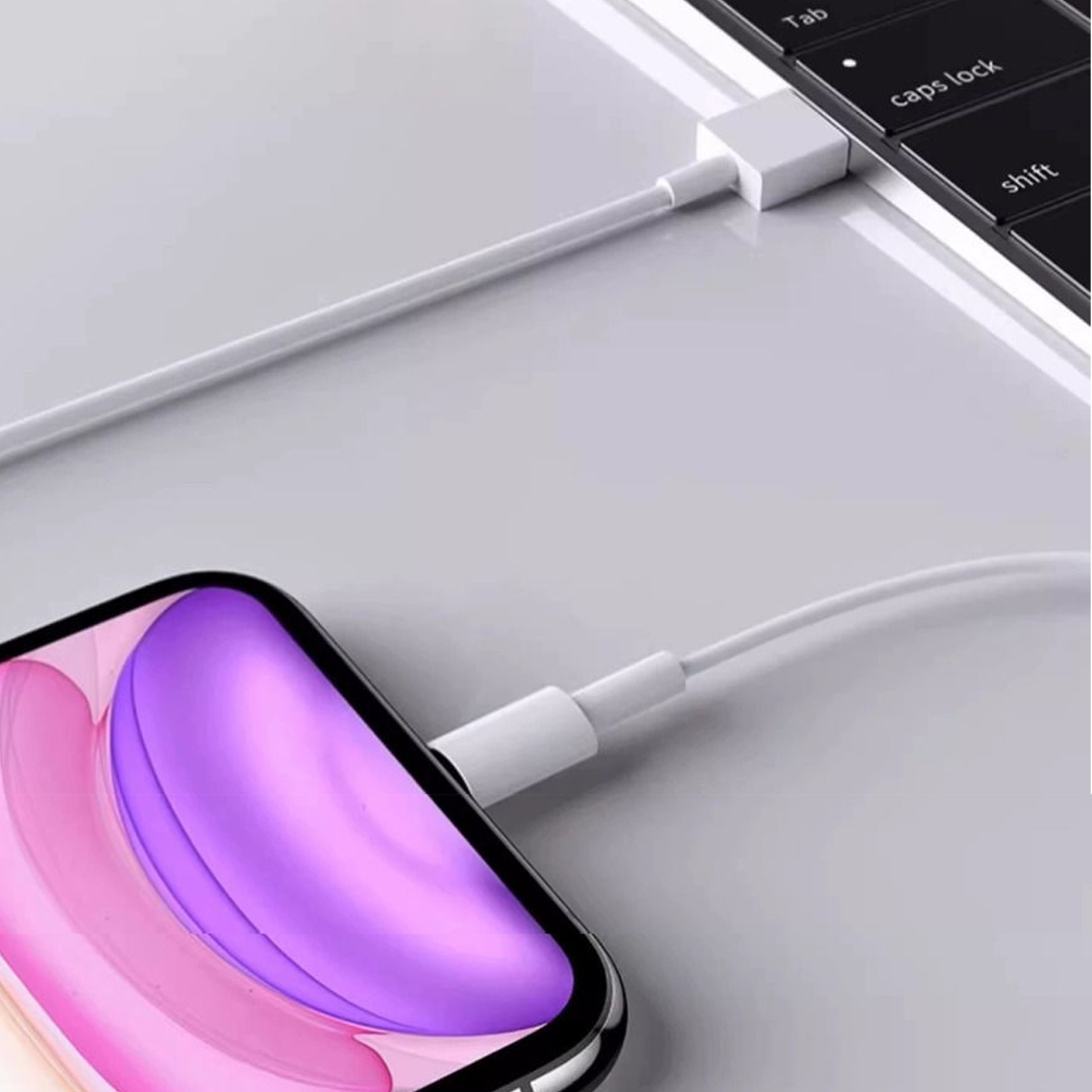 Ein weißes Ladekabel verbindet ein Telefon mit lila und rosa Bildschirm mit einem Laptop. Das Telefon ist im Vordergrund.