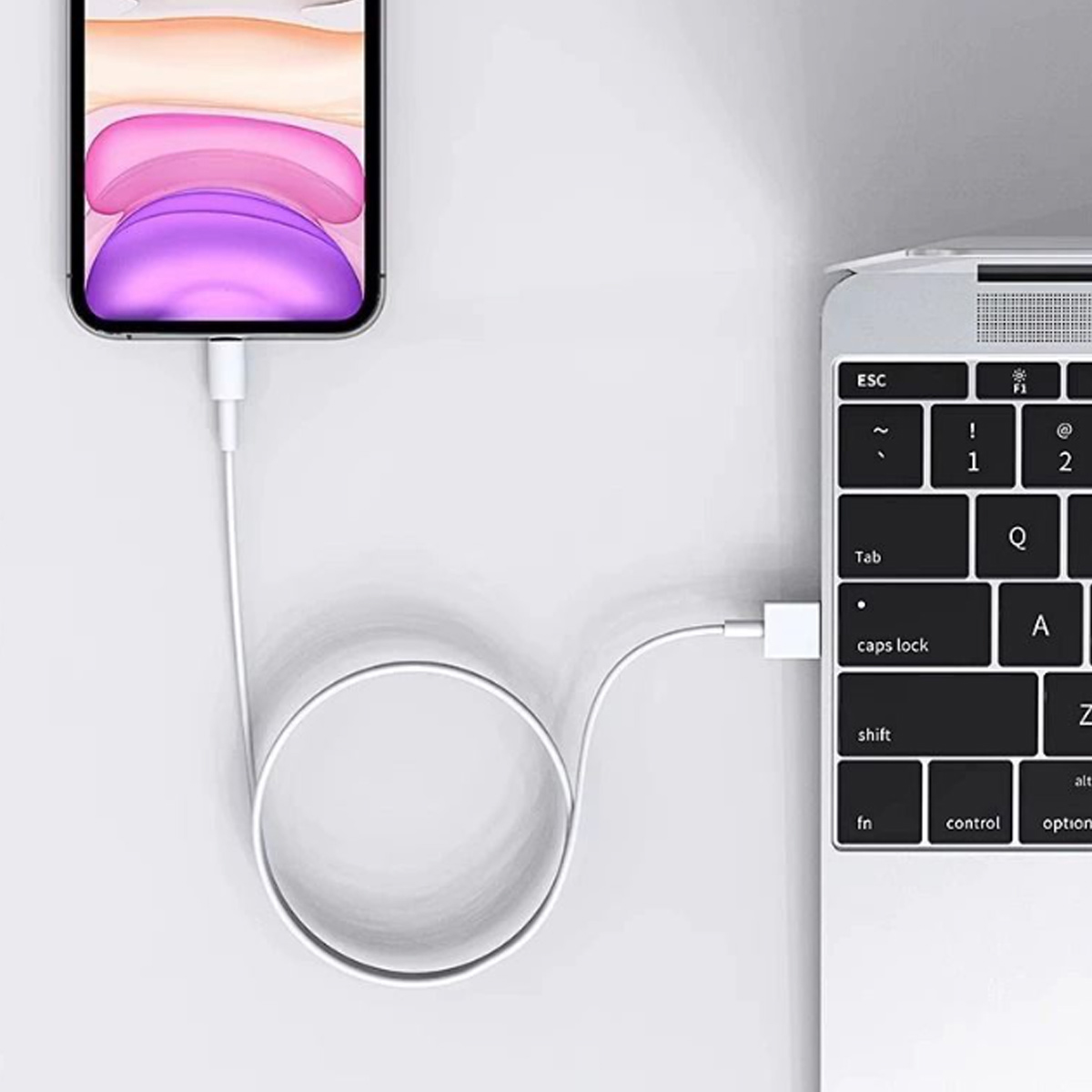 Ein Telefon, das mit einem weißen Kabel aufgeladen wird, das an einen Laptop angeschlossen ist. Der Telefonbildschirm zeigt einen lila und weißen Farbverlauf.