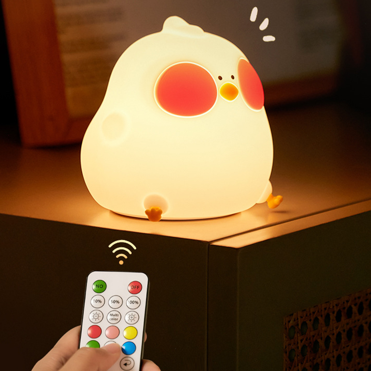 Eine kükenförmige Lampe steht auf einem Tisch. Eine Fernbedienung ist in einer Hand. Die Lampe ist weiß mit roten Wangen und gelben Füßen.