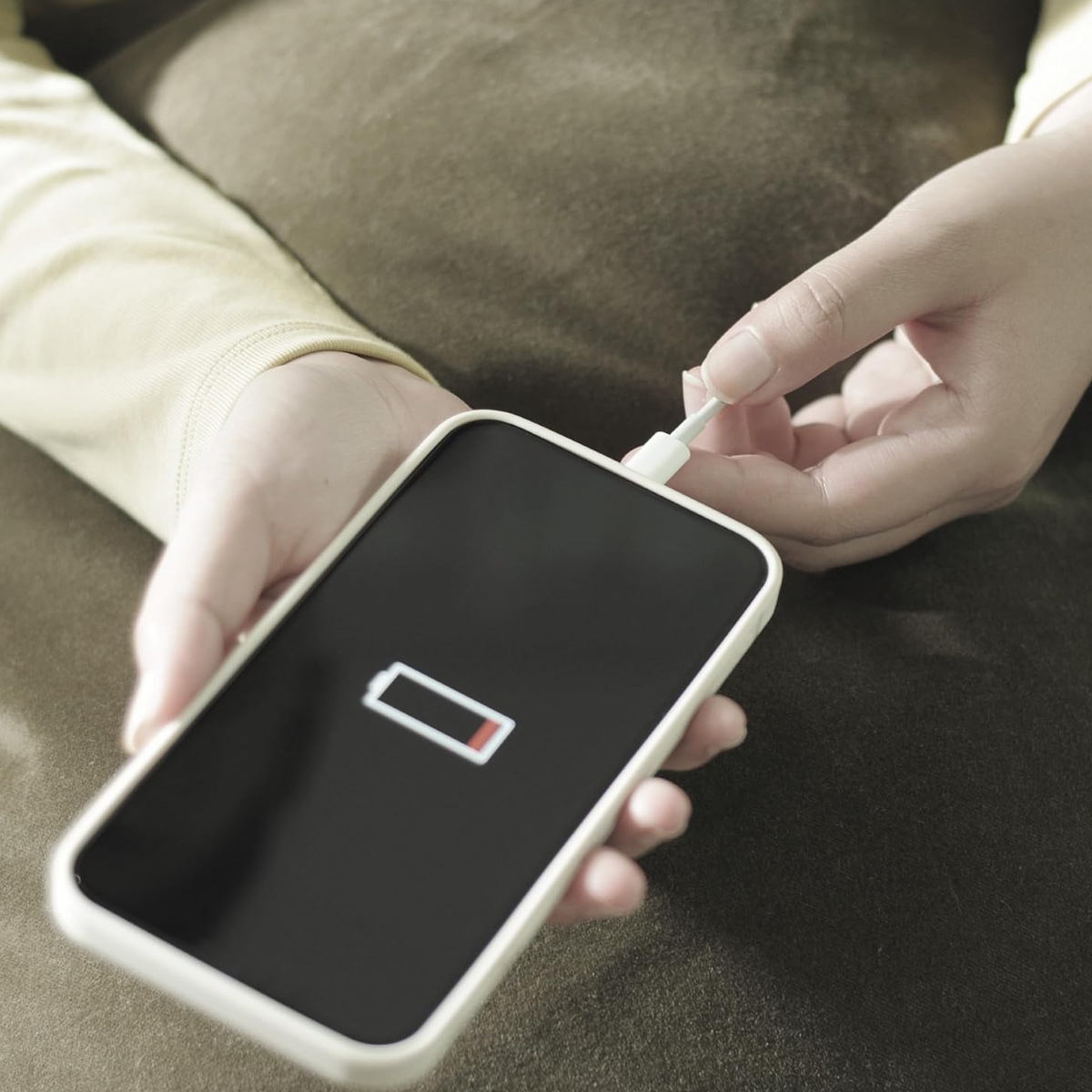 Eine Person steckt ein Ladegerät in ein Smartphone mit einer Anzeige für schwache Batterie auf dem Bildschirm. Das Telefon ist weiß.