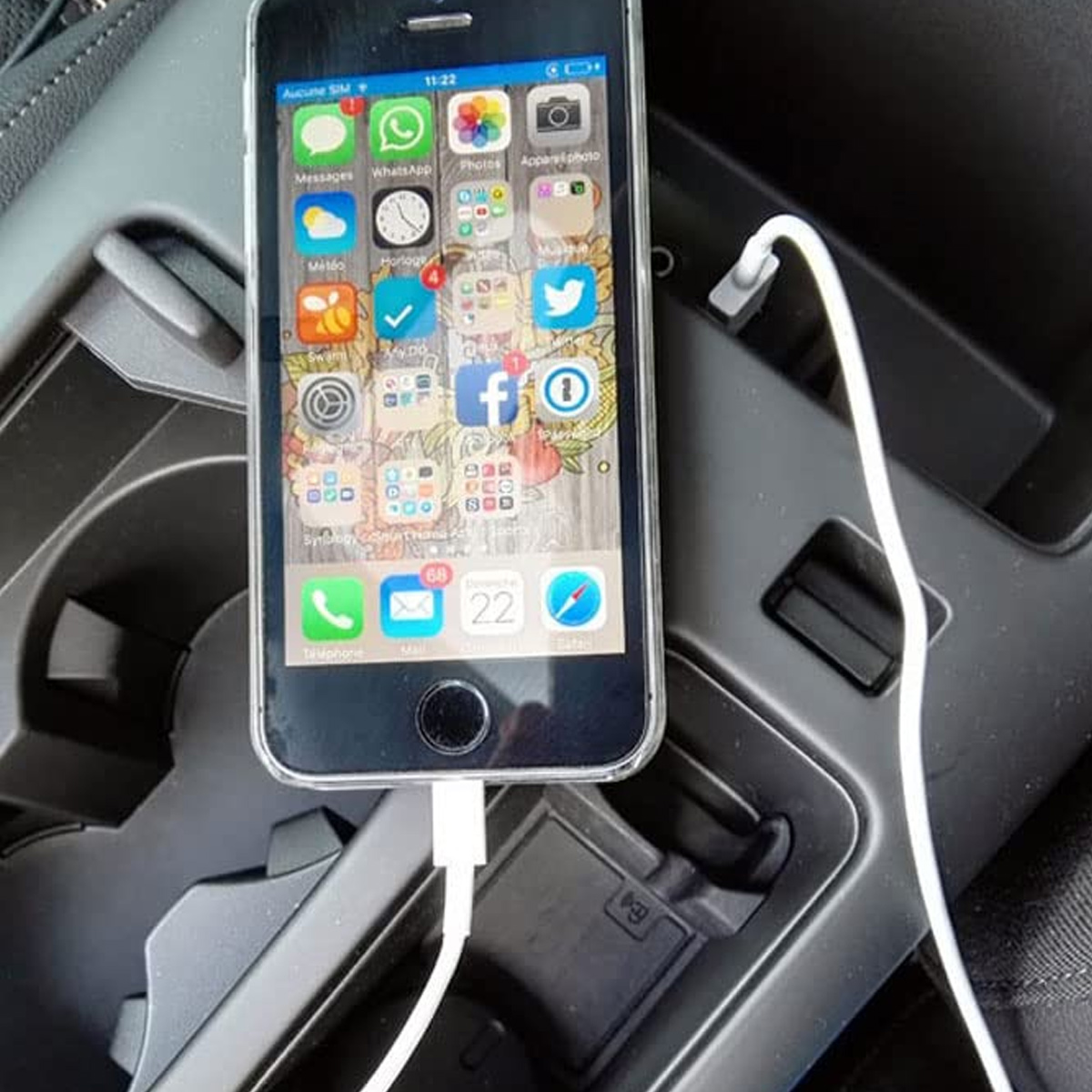 Ein iPhone wird in der Mittelkonsole eines Autos aufgeladen. Auf dem Telefon werden App-Symbole angezeigt. Ein weißes Ladekabel ist am Telefon angeschlossen.